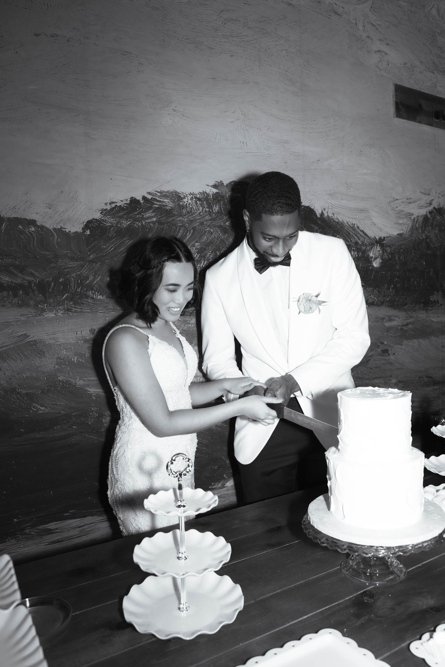 Couple cuts their wedding cake together in black and white photography.
