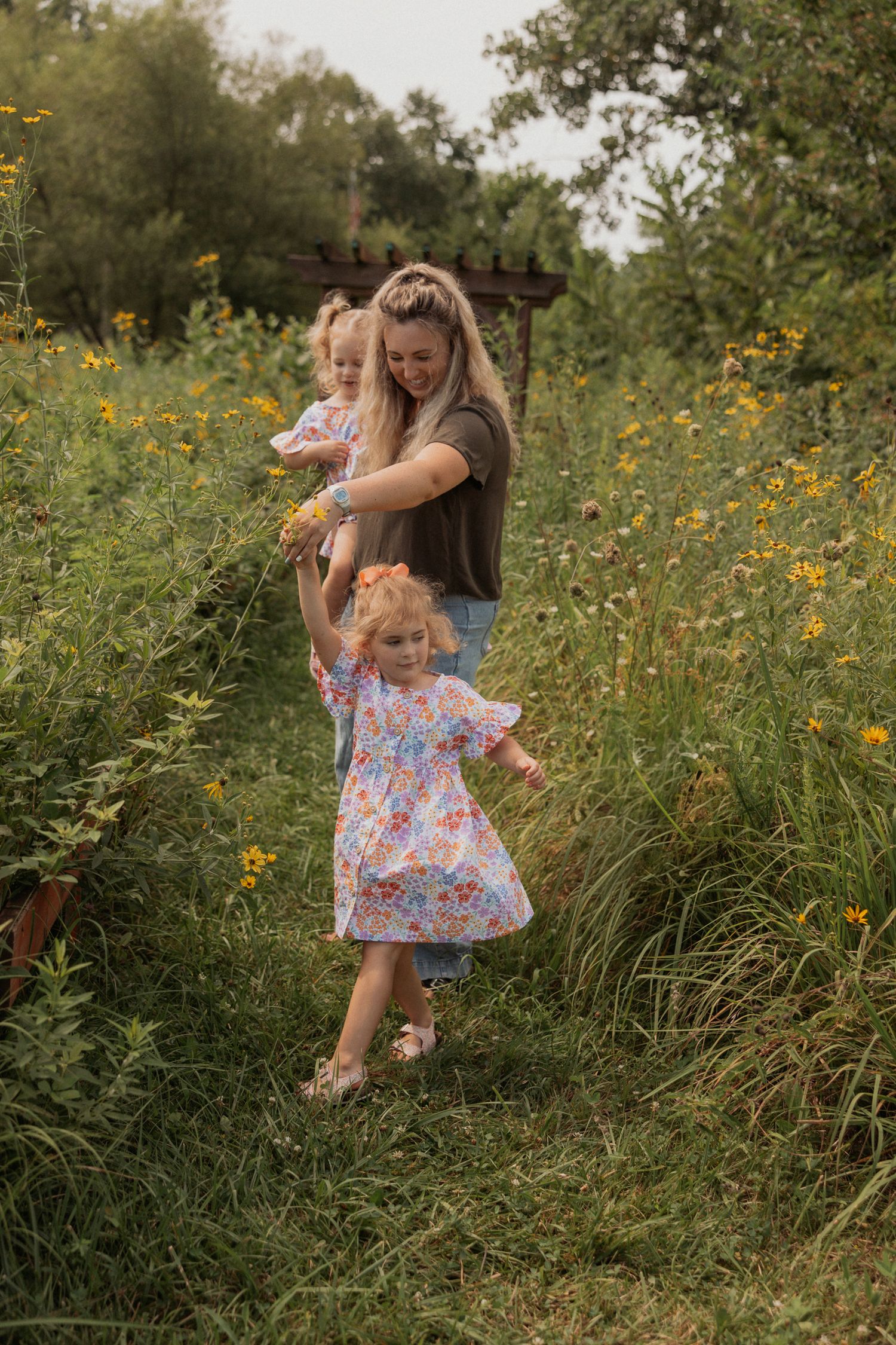 Family enjoying a playful moment together in a wildflower field with wooden pergola.