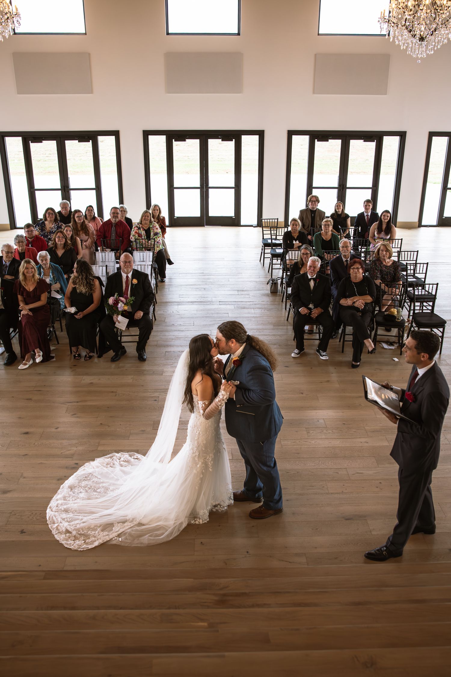 Wedding ceremony in progress in modern venue with hardwood floors and chandelier.