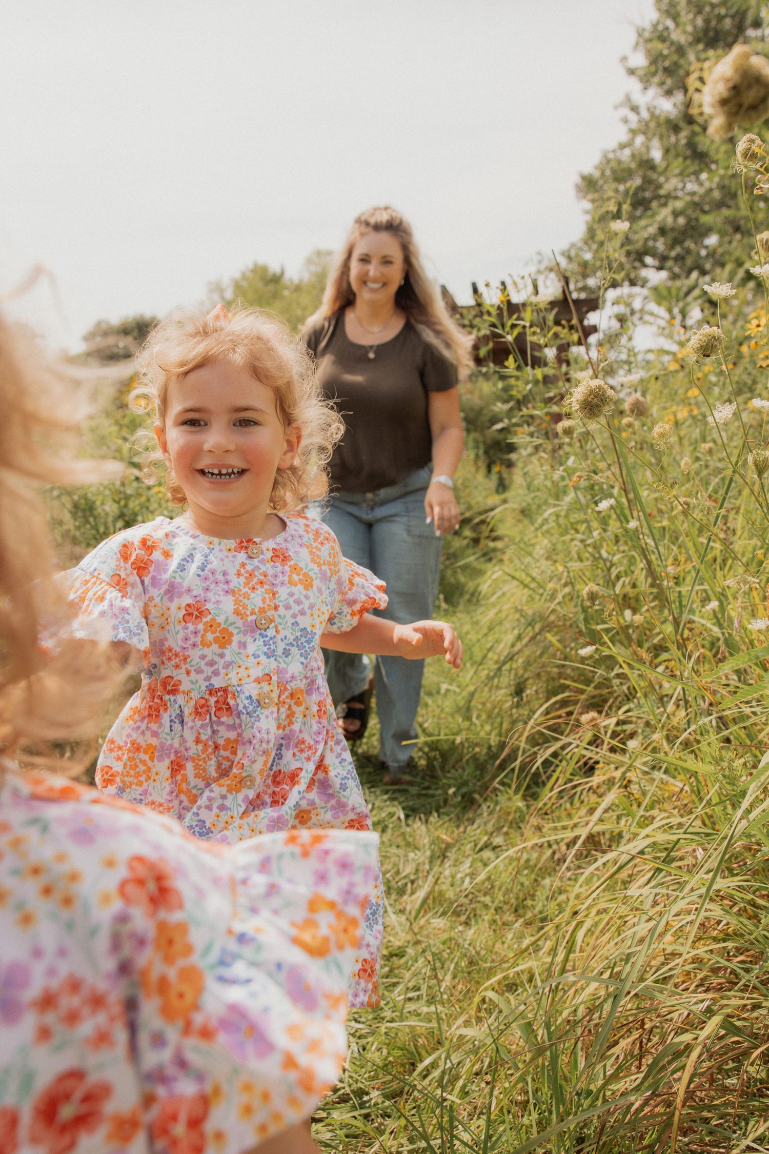 A joyful child in a floral dress plays in a meadow of tall grass.