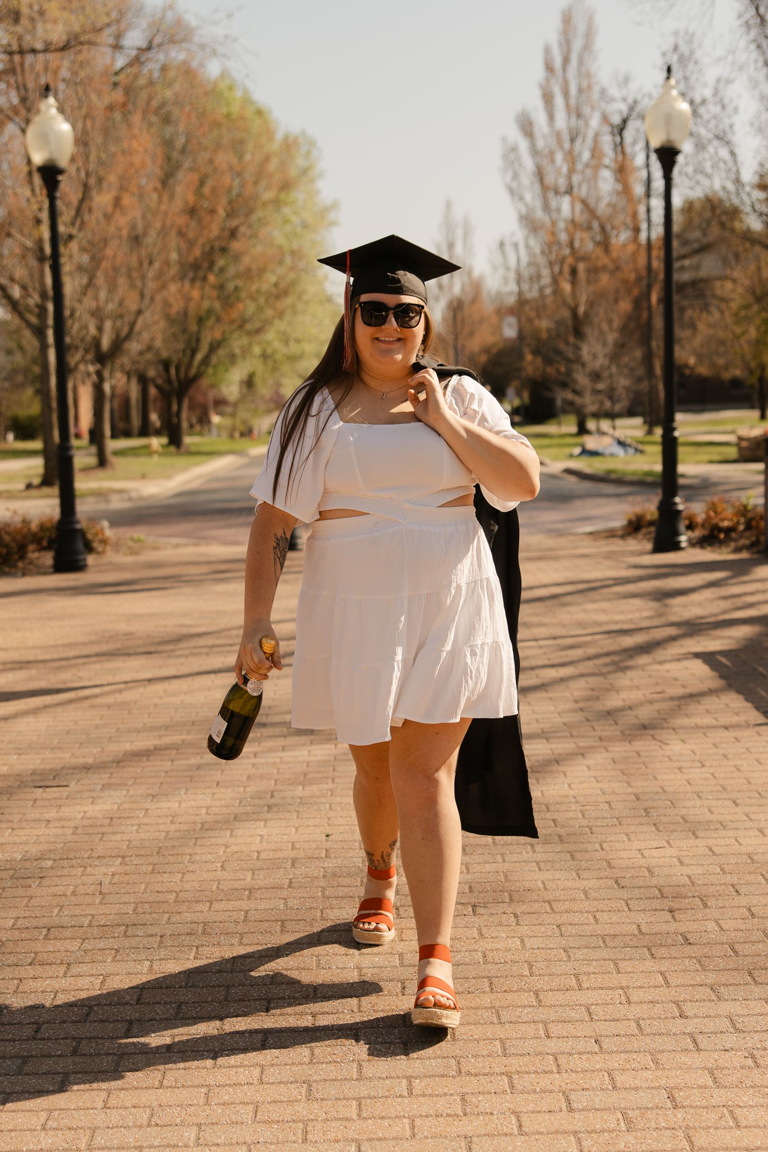 Someone in graduation attire poses playfully on a brick pathway.