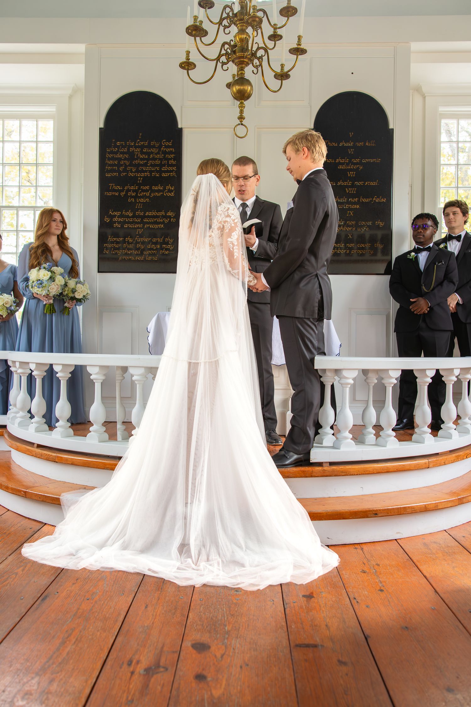 Wedding ceremony in historic chapel with wooden floors and elegant chandelier.