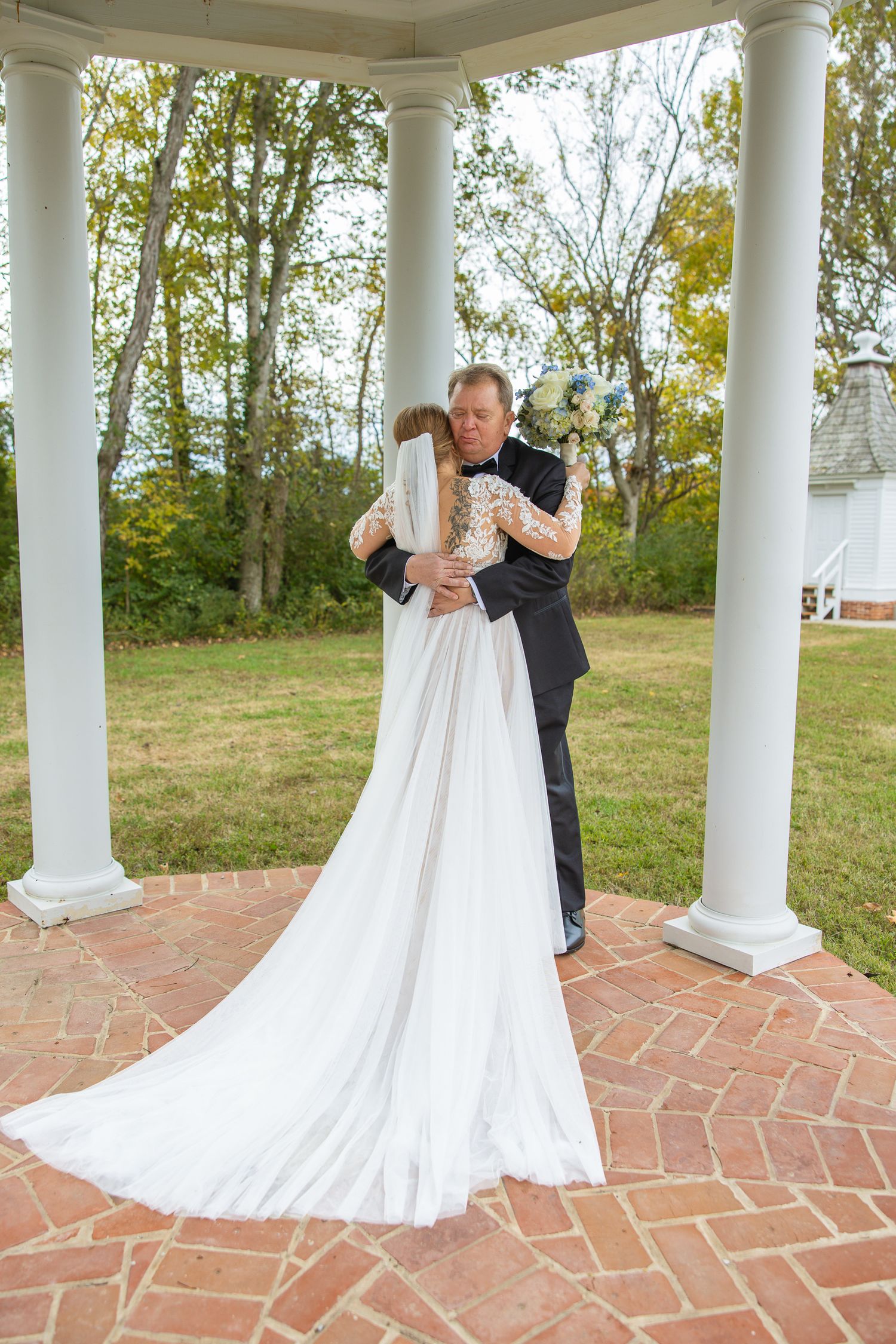 Sweet embrace captured in white gazebo with classic columns and brick flooring.