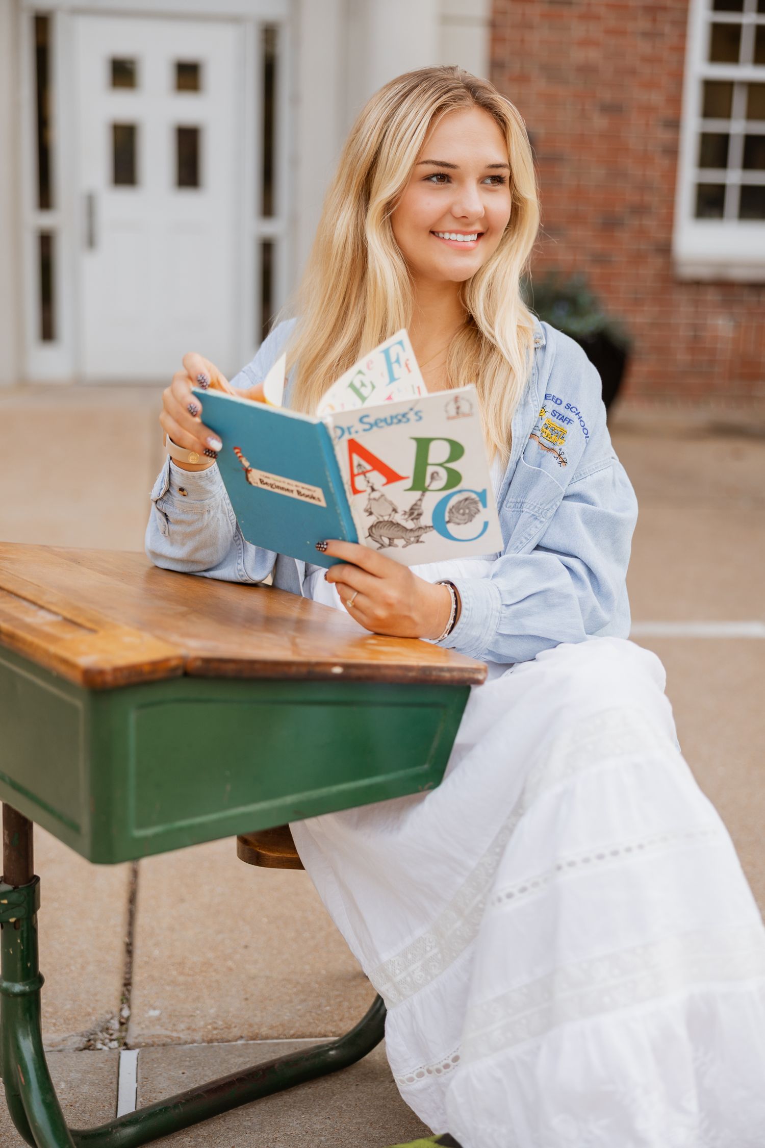Someone reads a colorful ABC book while seated at a vintage green school desk outdoors.