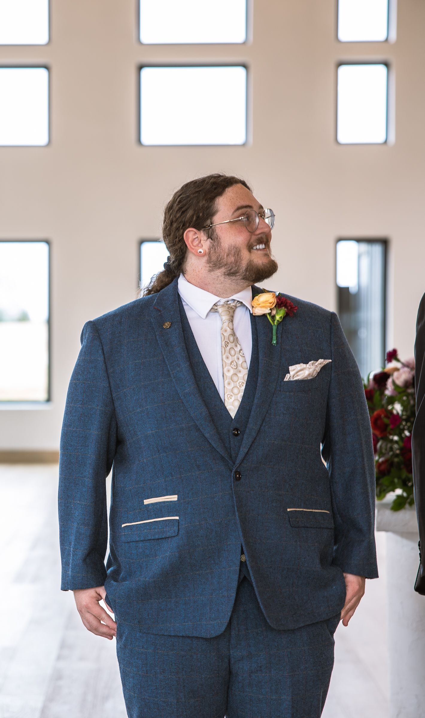 Two people in matching navy suits share a candid moment at wedding venue.