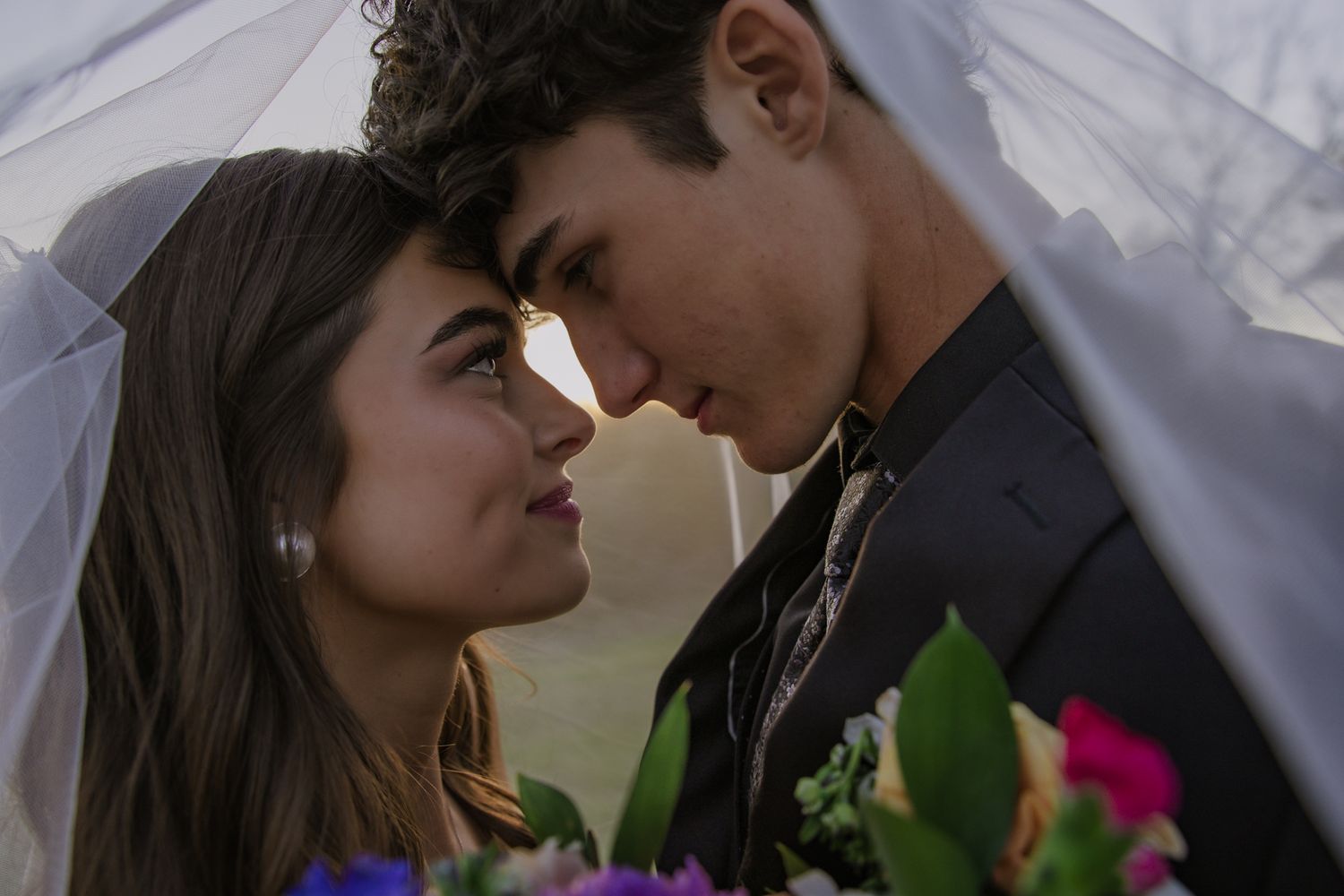 Romantic moment captured under a floral arch during outdoor wedding ceremony.