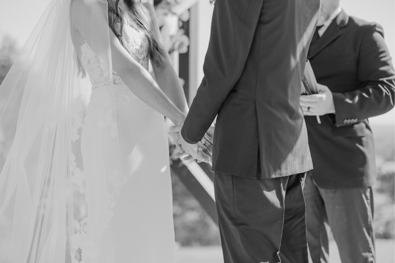 A couple stands close together under a clear umbrella in formal wedding attire.