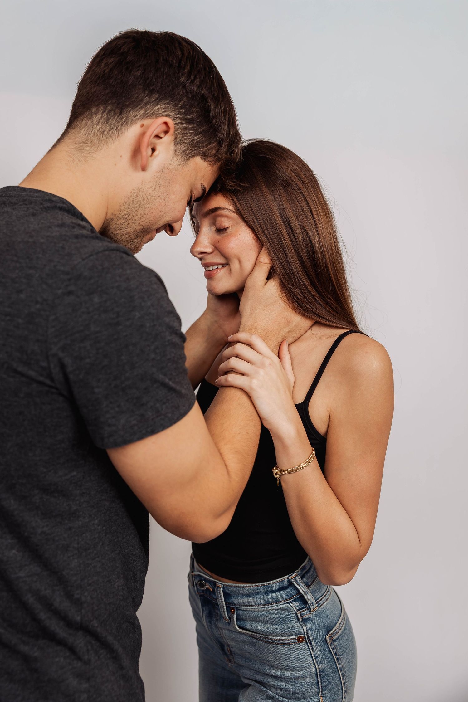 Playful couple laughing and embracing in casual outfits against white backdrop.
