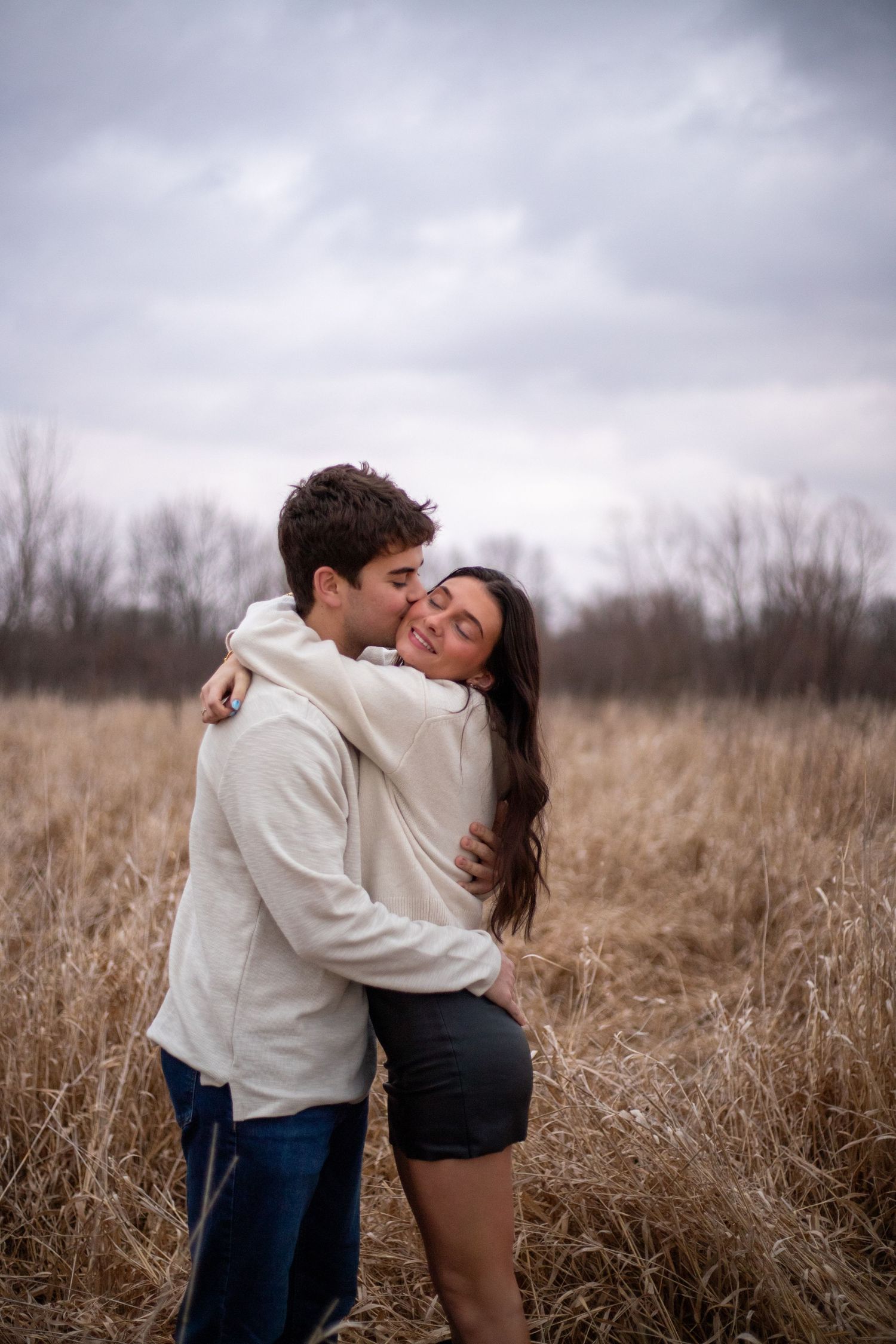 Romantic couple embracing in tall grass field on cloudy day.