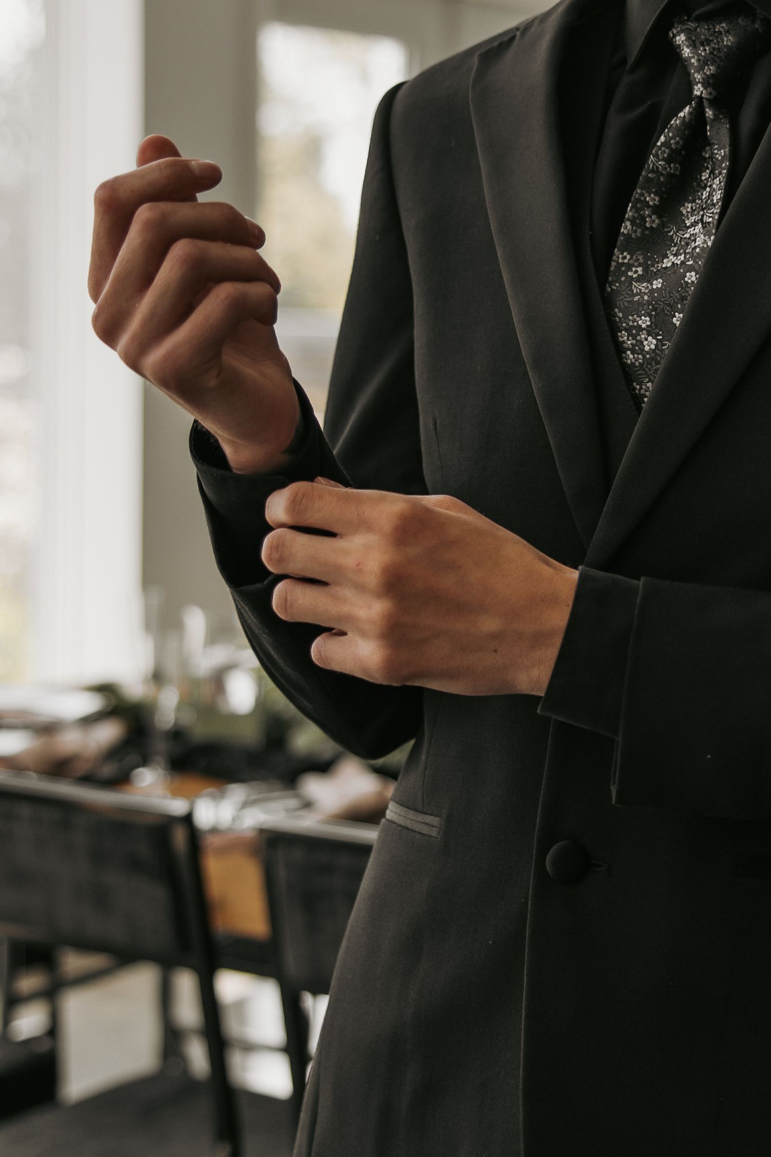 Close-up of hands adjusting sleeve cuff on black formal suit jacket.