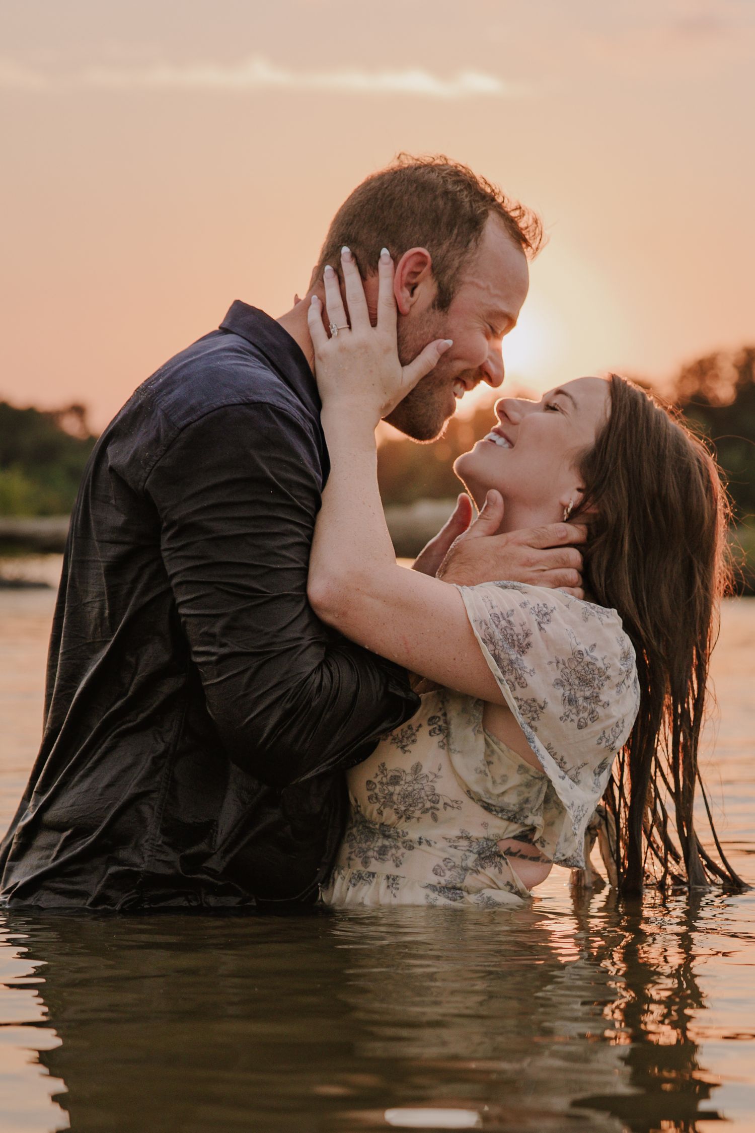 Romantic couple embracing in water during sunset with dramatic lighting.