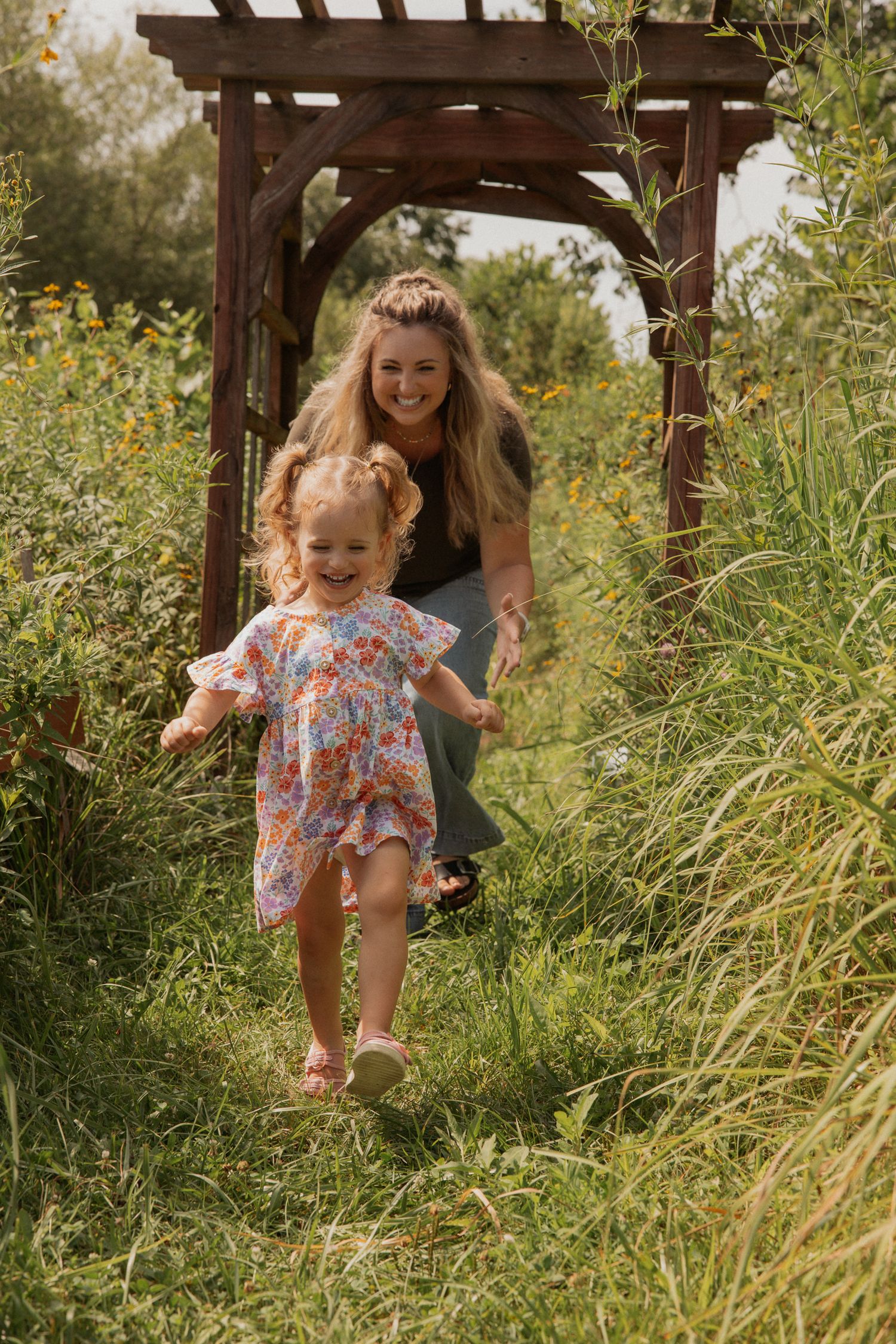 A playful scene unfolds beneath a wooden pergola surrounded by wild grasses.