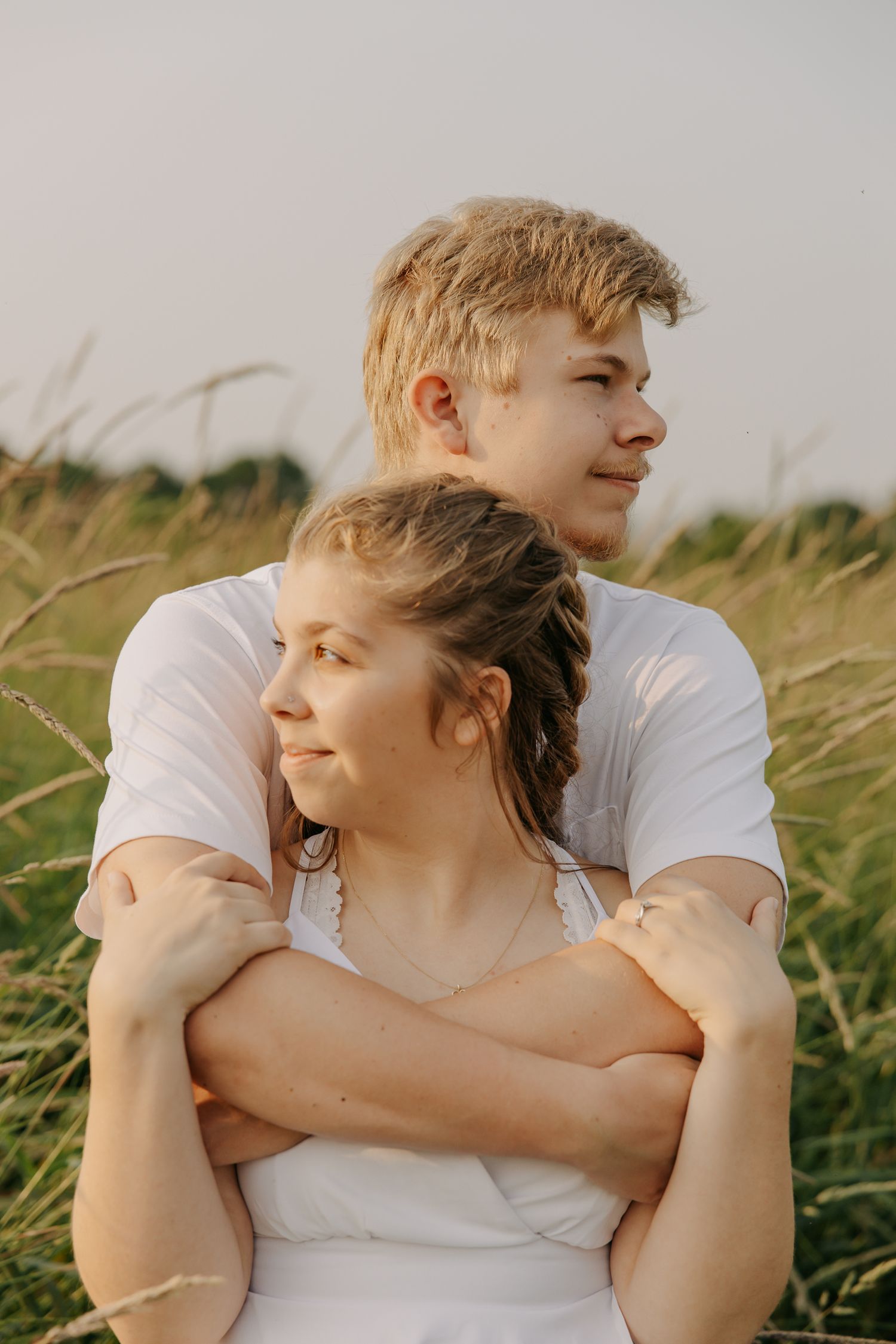 A couple embraces in a field of tall grass during golden hour.
