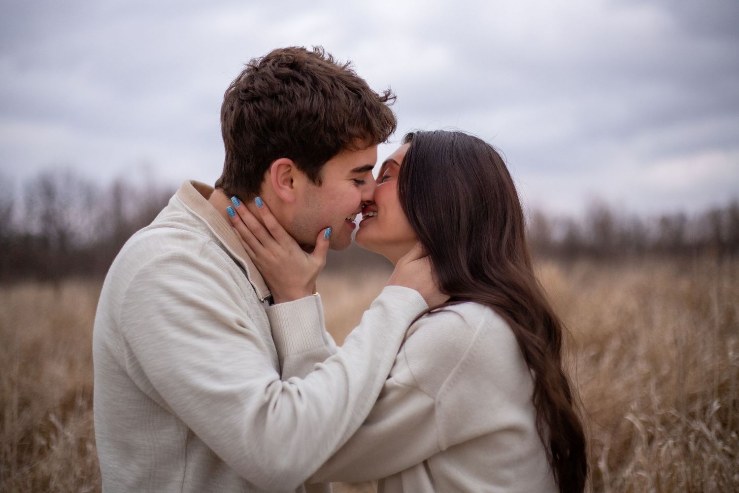 Romantic couple sharing intimate moments in a misty field with overcast sky.