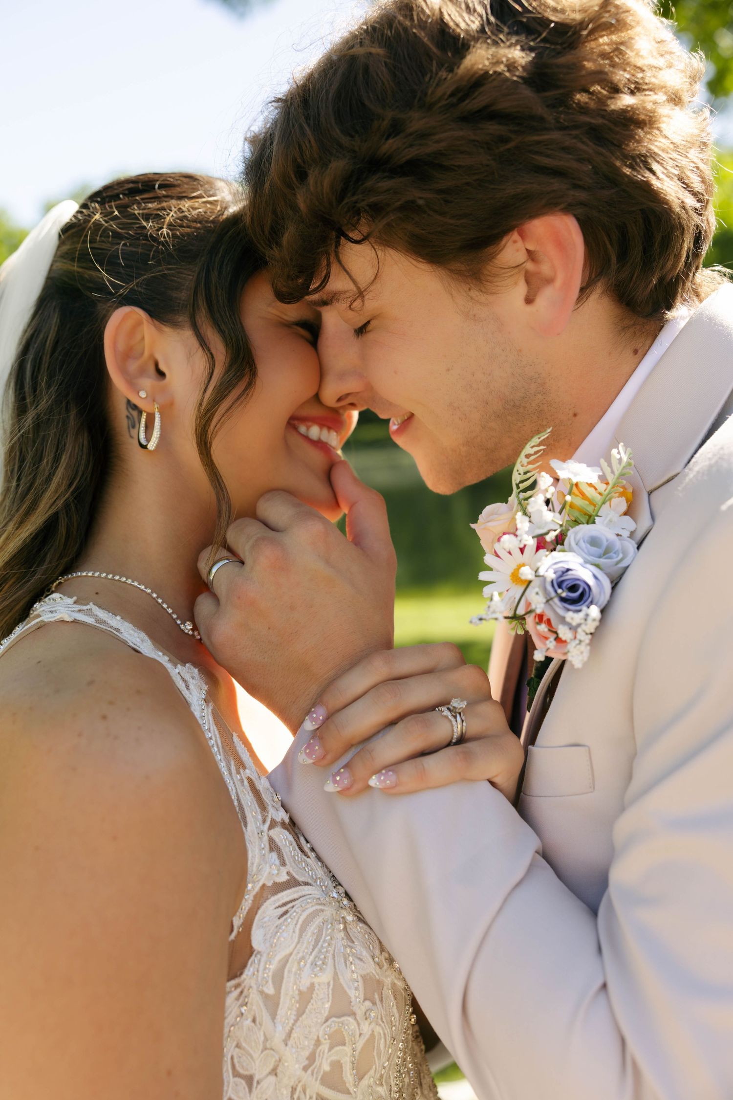 A bride and groom share an intimate nose-to-nose moment outdoors, smiling joyfully on their wedding day.