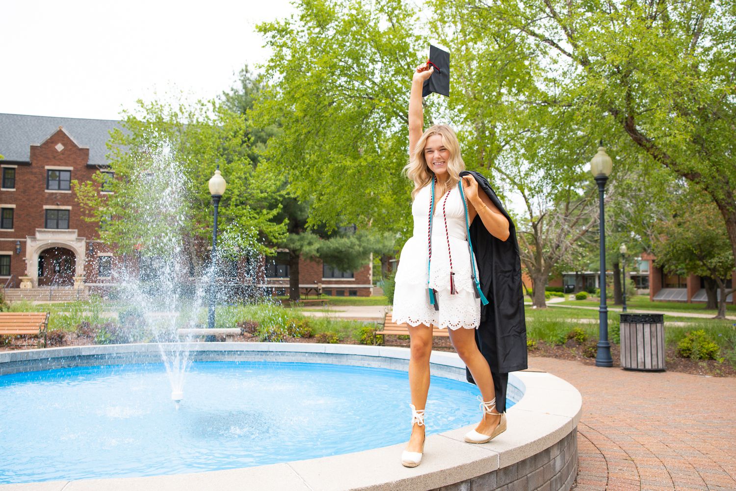 Scenic campus walkway with trees, fountains and brick buildings on a sunny day.