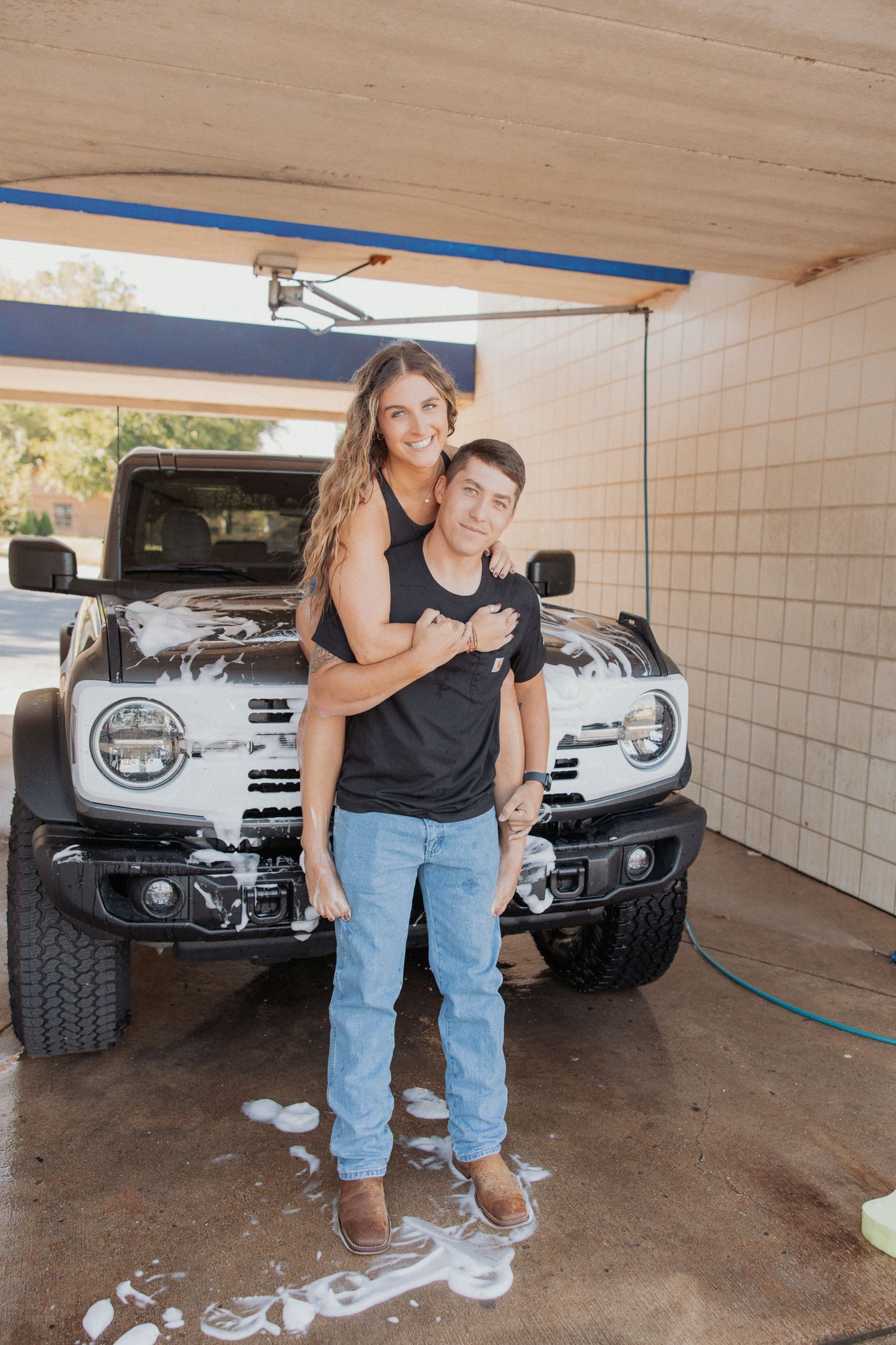 Two people share an intimate moment while standing in a garage with a silver vehicle behind them.