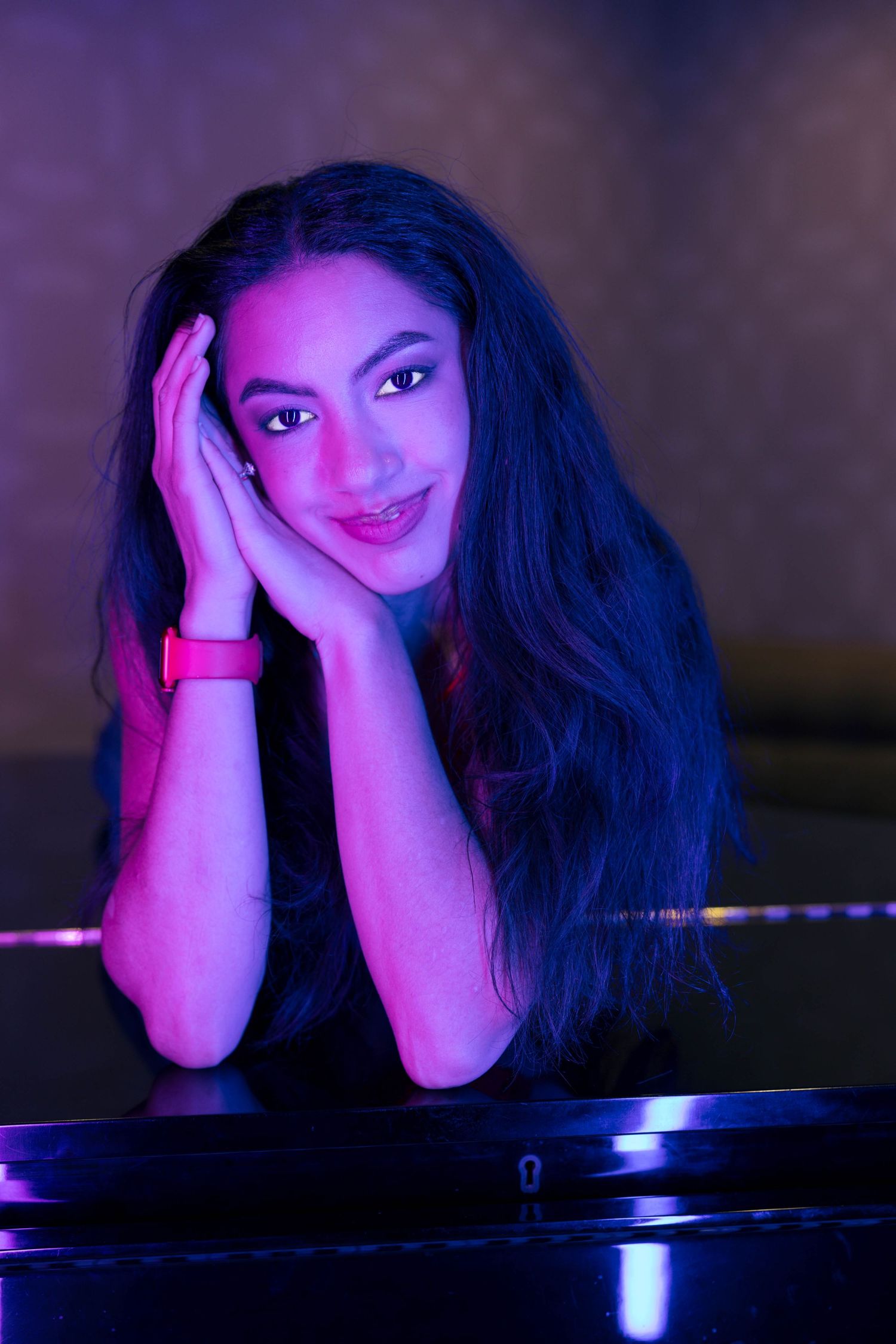 Young woman with long dark hair resting her face on her hands under purple neon lighting.