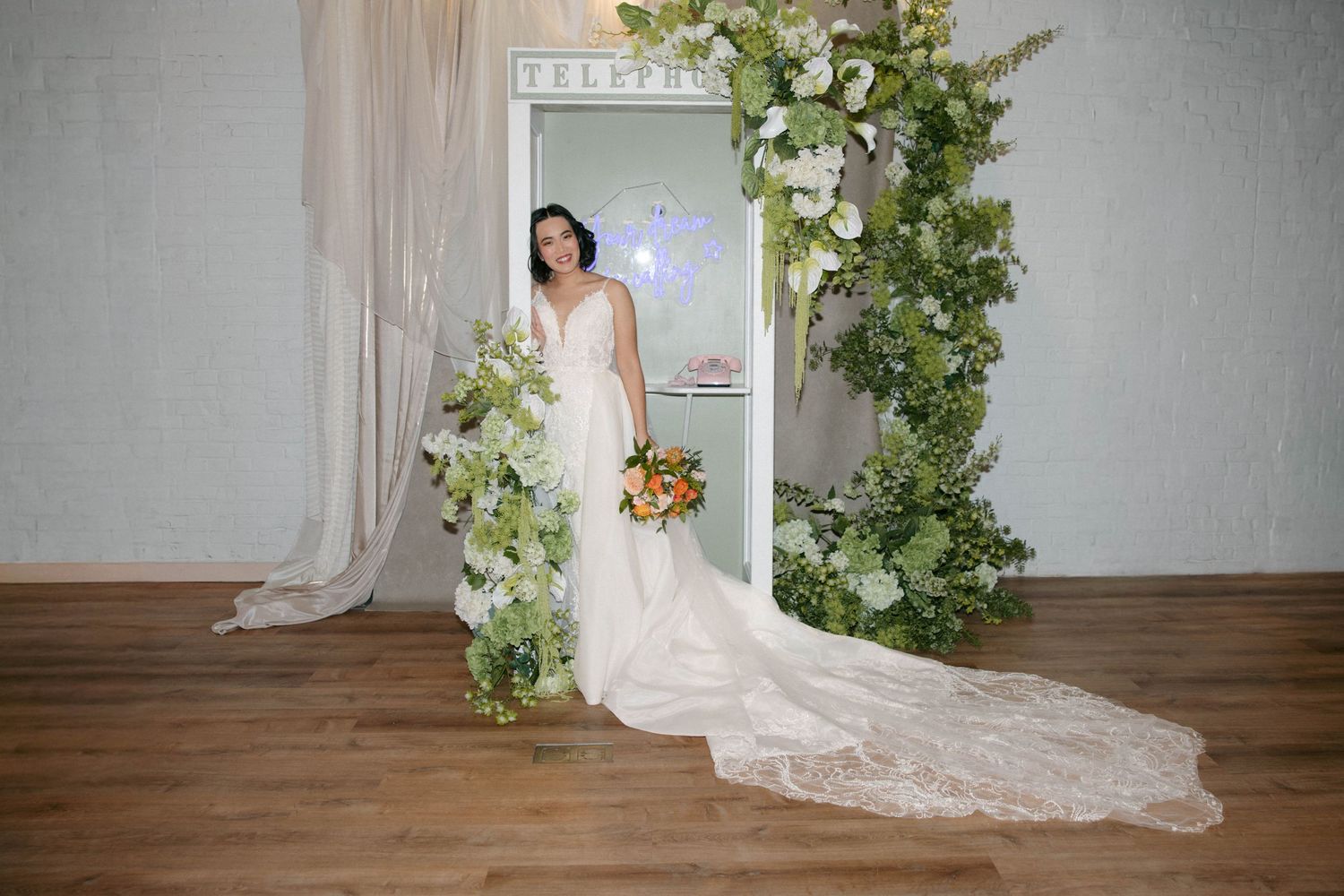 Wedding photo backdrop with greenery and white curtains in an indoor setting.