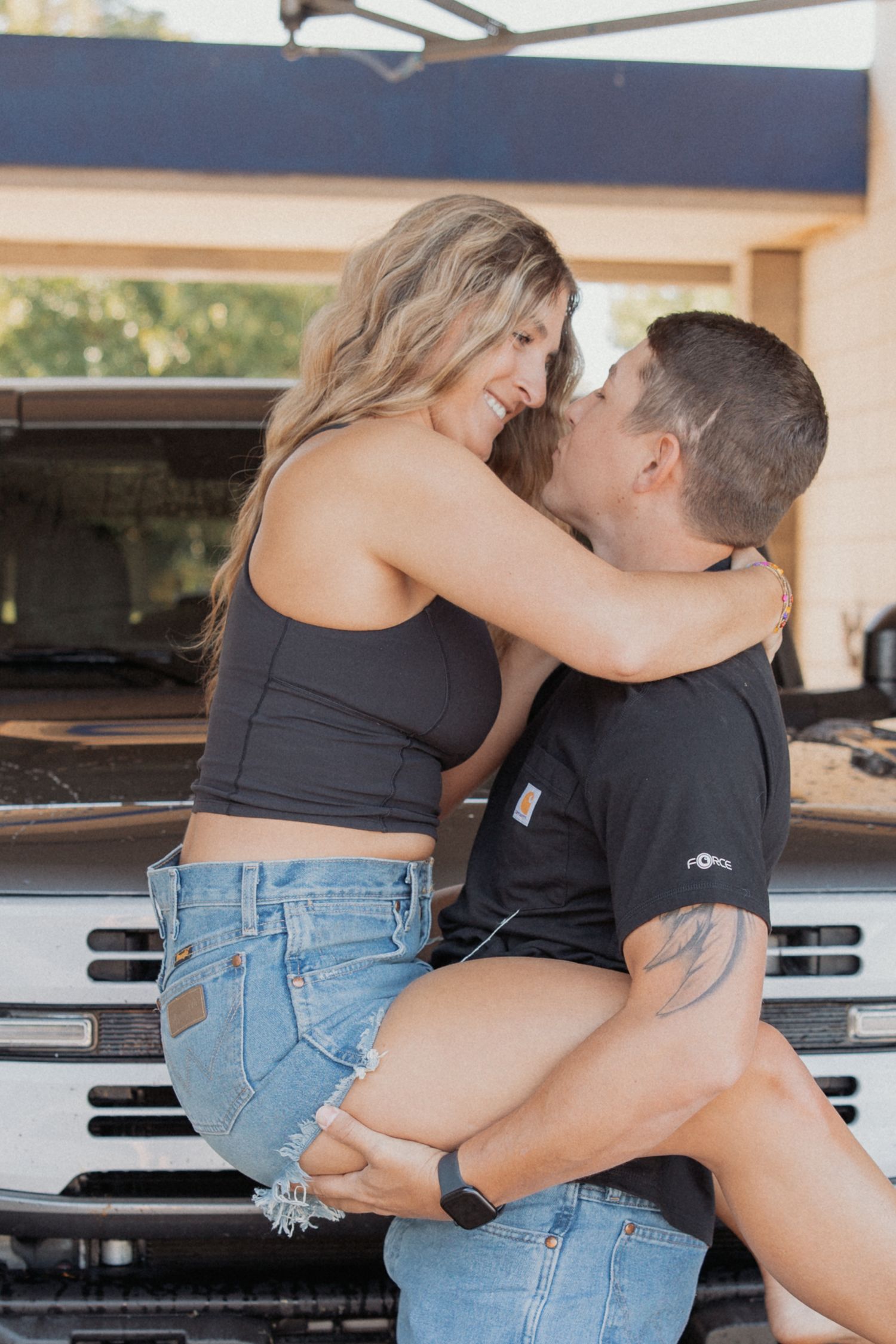 Couple in denim and dark tops sharing romantic moment by parked truck.