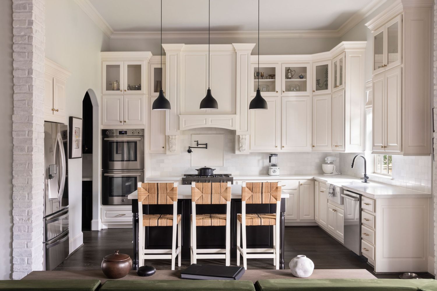 Modern white kitchen with wood accents features pendant lights, marble countertops, and a long dining area.