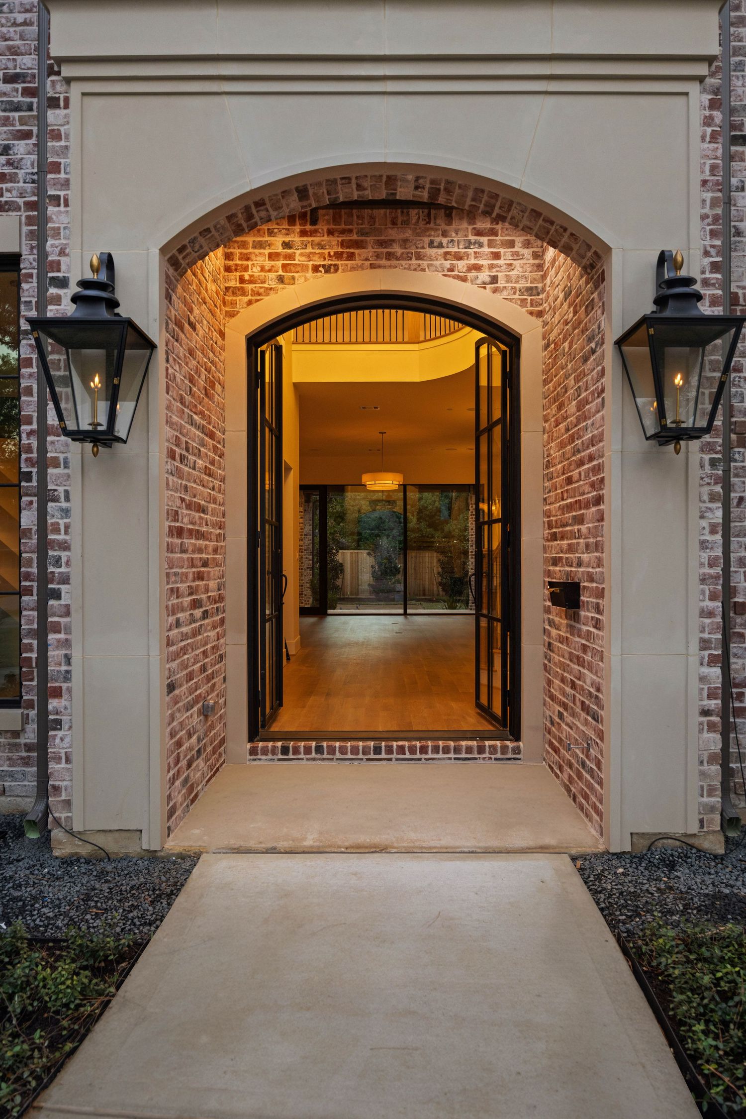 Brick-framed garage entrance with arched design and exterior lighting at dusk.