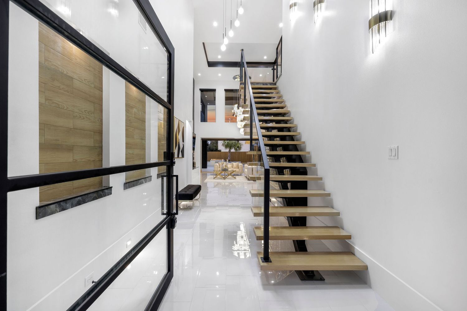 Modern floating staircase with black railings and wooden treads in a bright white hallway with high ceilings.