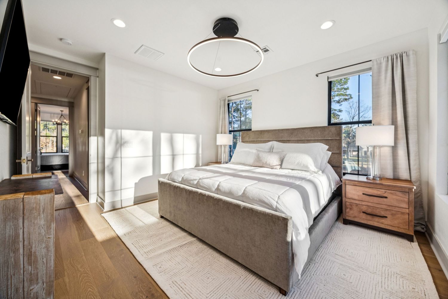 Bright contemporary bedroom with gray upholstered bed frame and large windows letting in natural light.