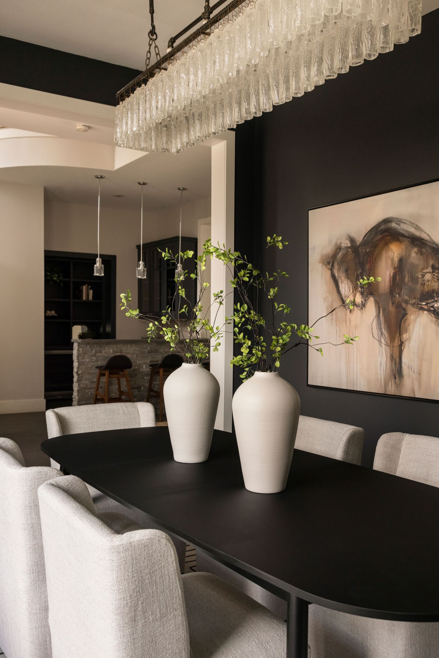 Dining room with crystal chandelier, black table, and white vases featuring green plants.