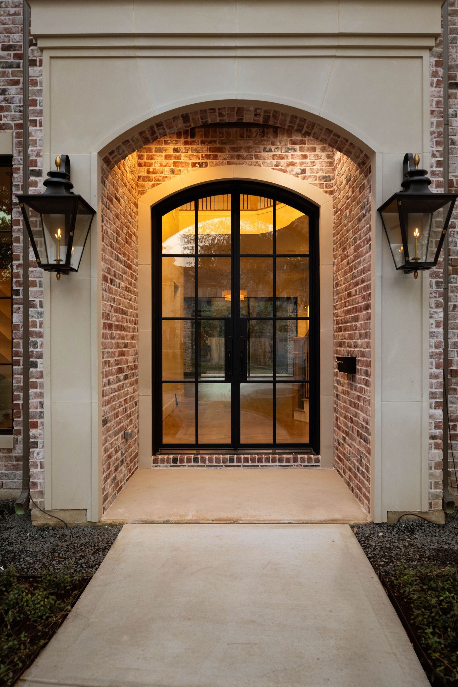 Illuminated garage entrance with arched brick detailing and black-framed windows at twilight.