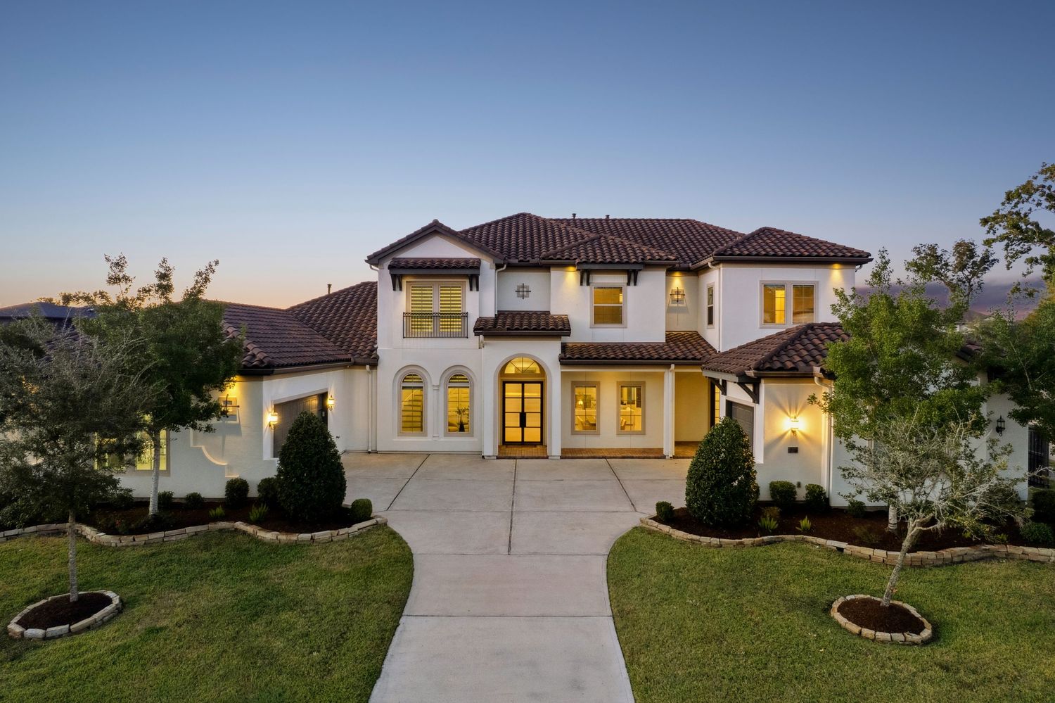 Mediterranean style luxury home exterior with dramatic front entrance lighting at night.