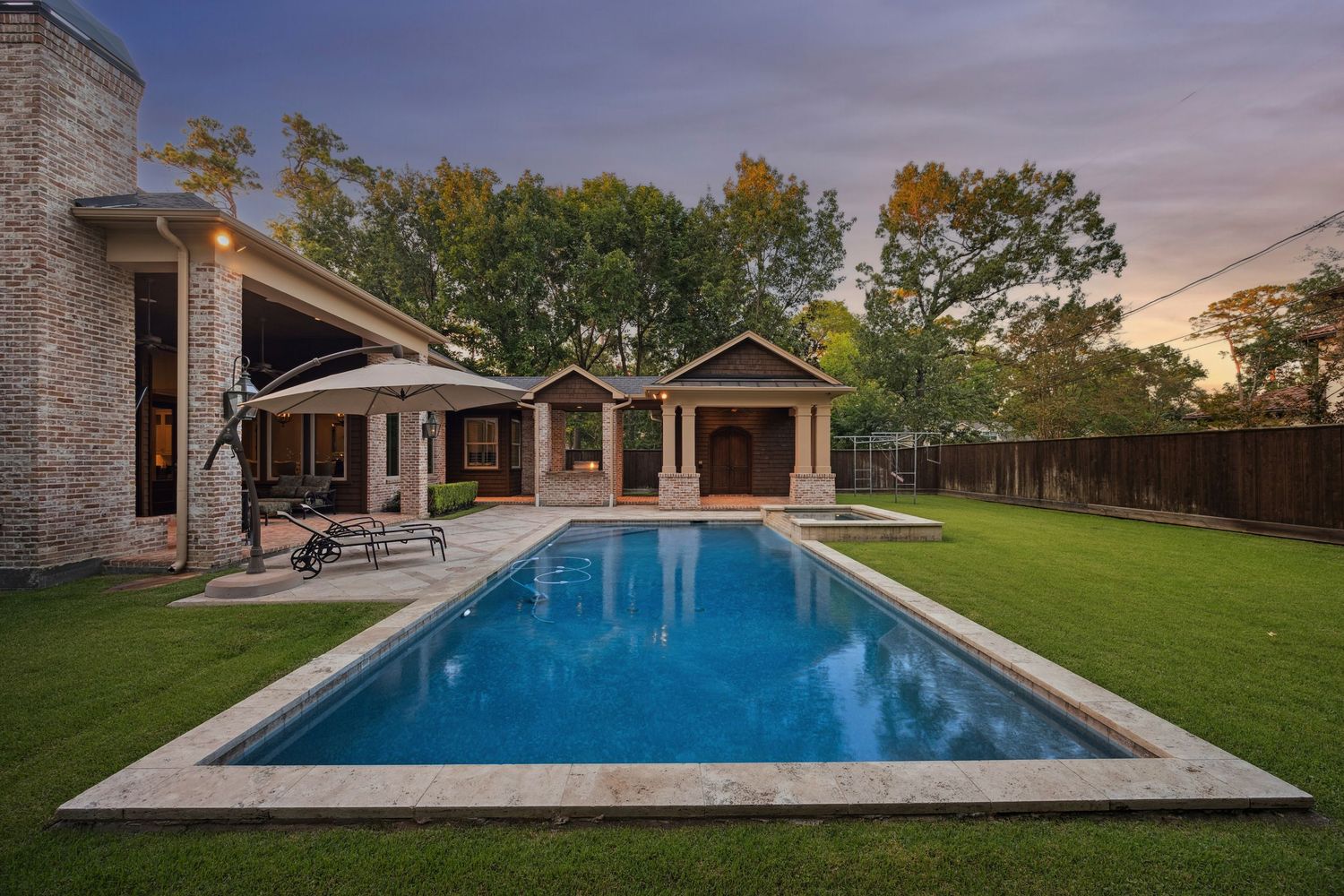 Panoramic view of a modern swimming pool with stone patio and manicured lawn.