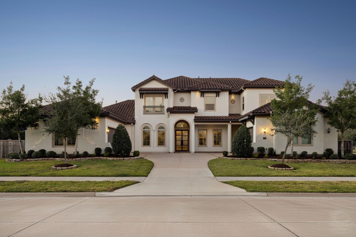 Front view of expansive Mediterranean-style home with circular driveway and manicured lawn.