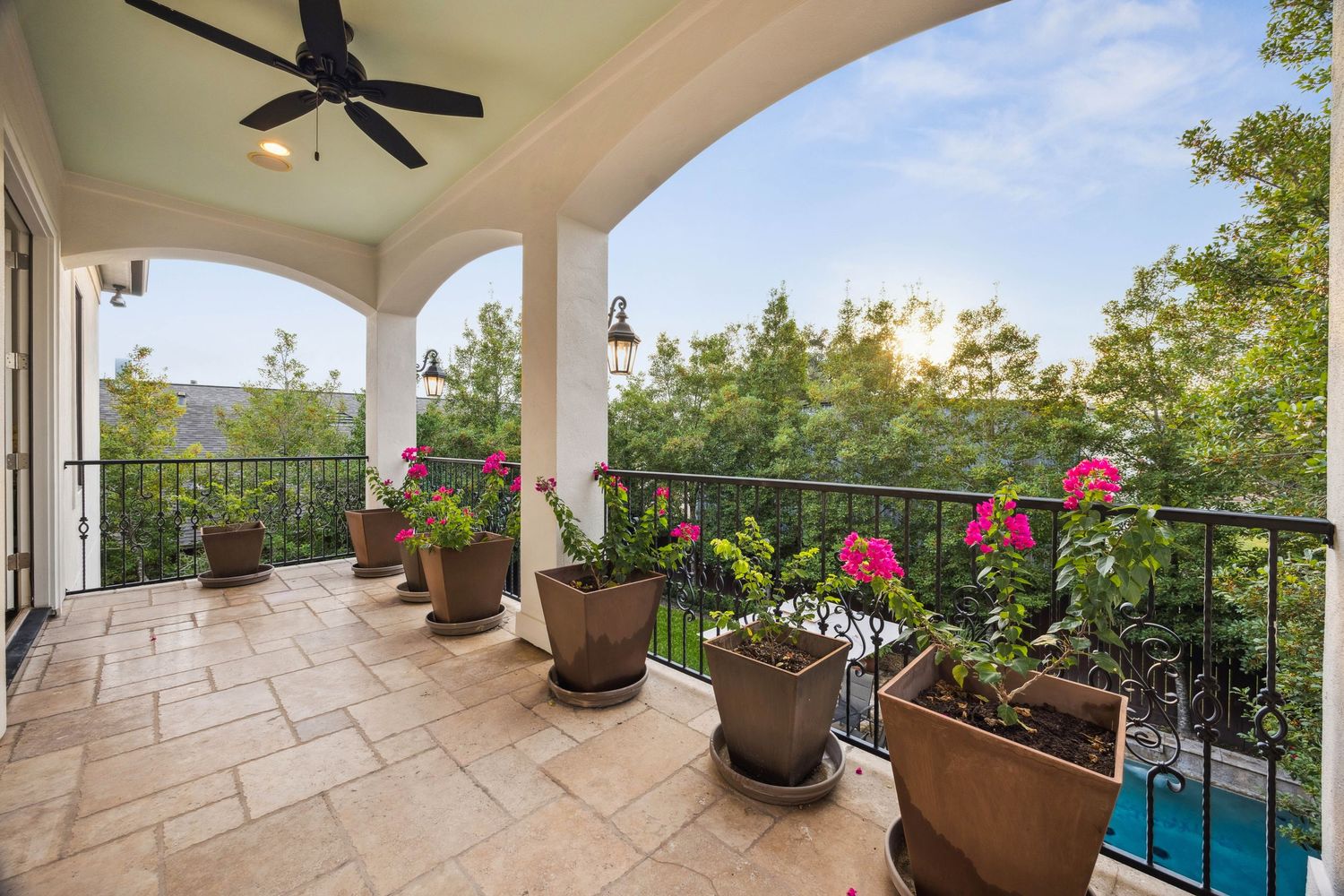 Covered patio with stone flooring, ceiling fan, and potted plants overlooking the backyard.