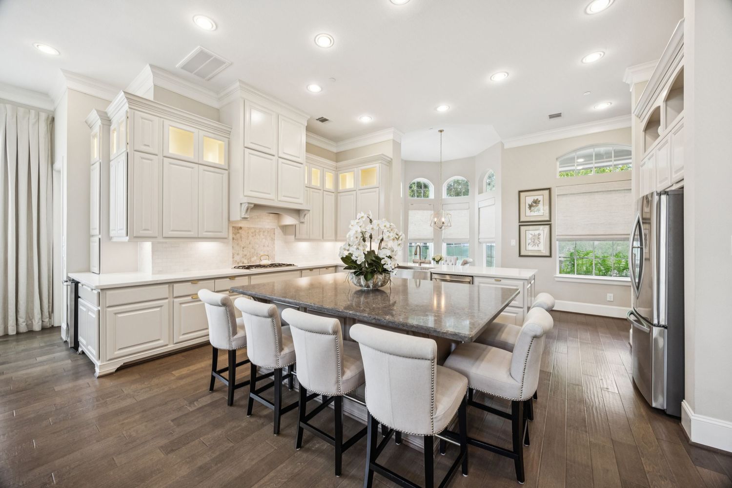 Contemporary white kitchen with bar seating, stainless appliances, and recessed lighting.