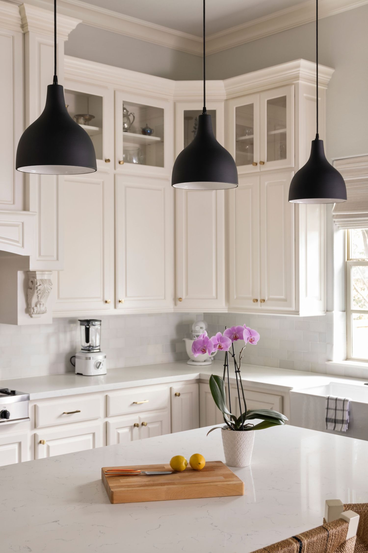 Modern white kitchen with black pendant lights, marble countertops, and a pink orchid centerpiece on the island.