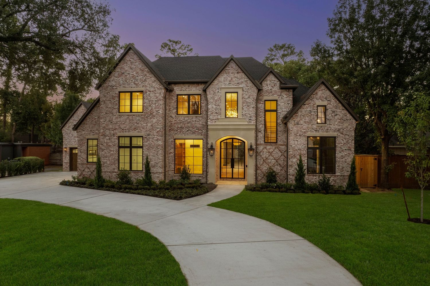 Modern farmhouse-style home with stone facade and illuminated windows in evening light.