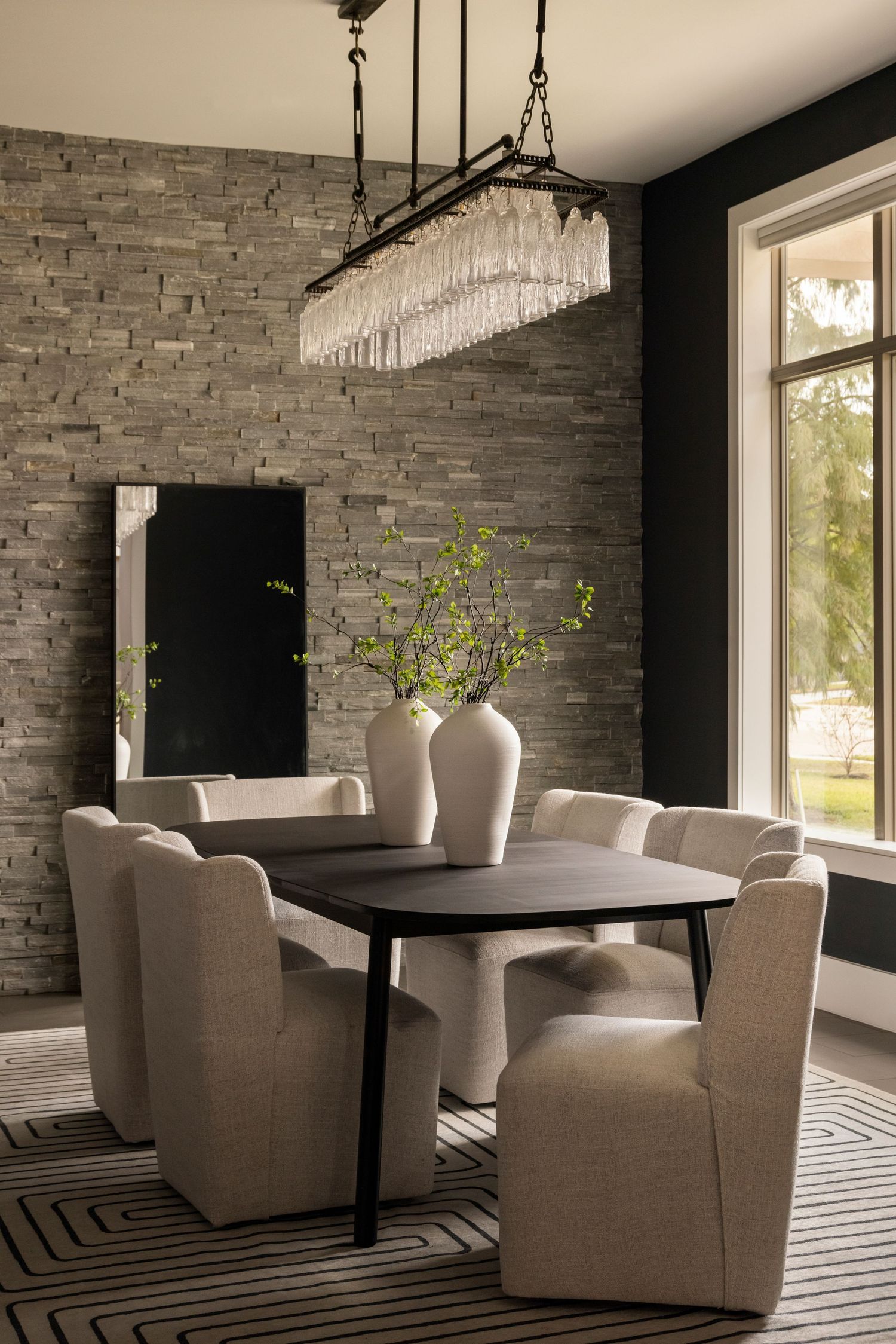 Stylish dining area with round table, upholstered chairs, and stone accent wall.