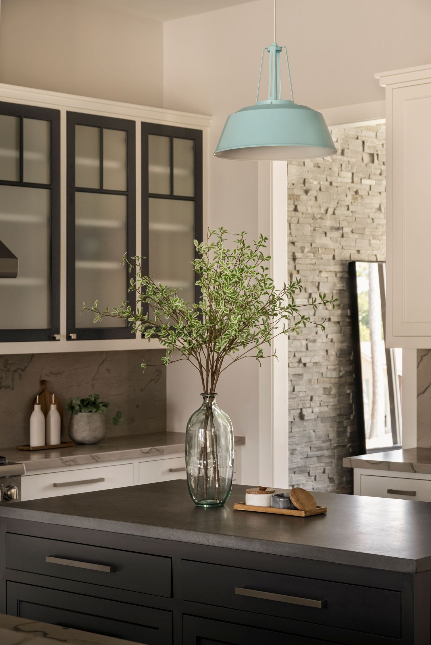 Modern kitchen with mint pendant light, black cabinets, and white stone accent wall.