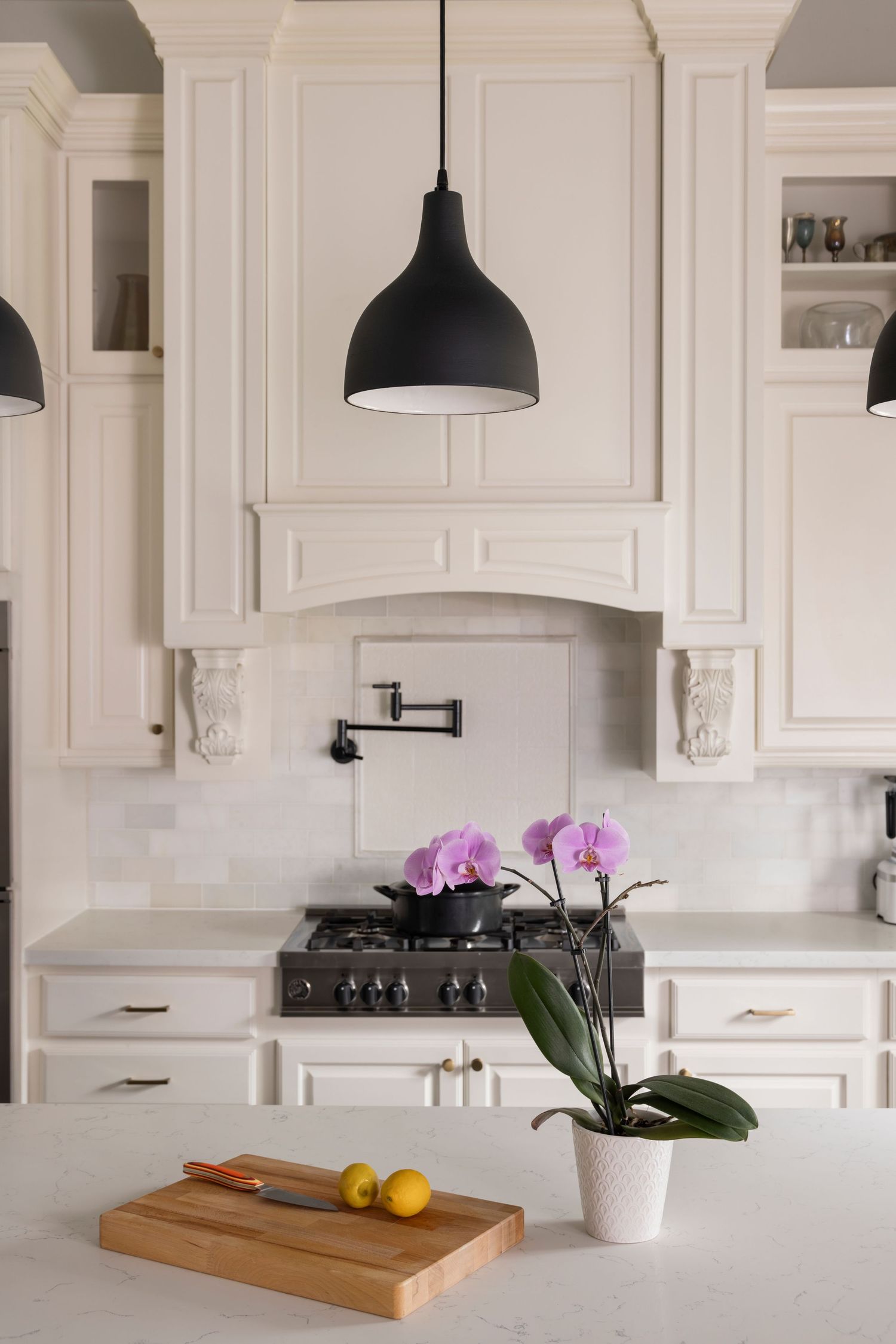 Modern white kitchen with black pendant light, marble counters, potted orchid and wooden cutting board with lemons.