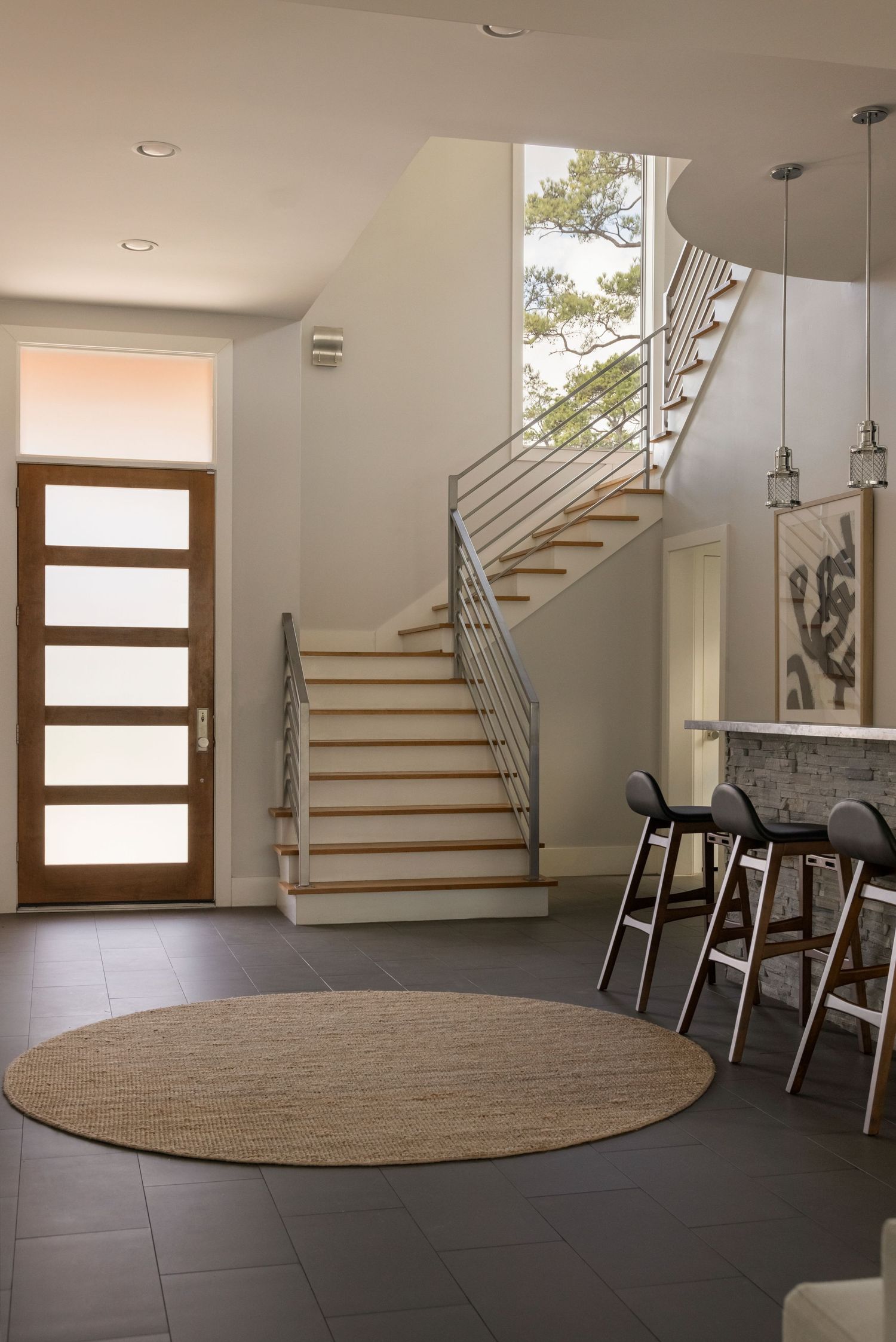 Modern entryway with wooden staircase, glass panels, and dark tile flooring.