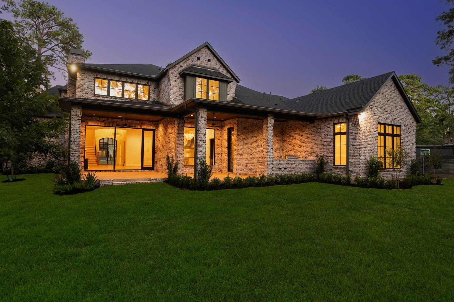 Luxury stone and brick home exterior with warm lighting at dusk and manicured lawn.