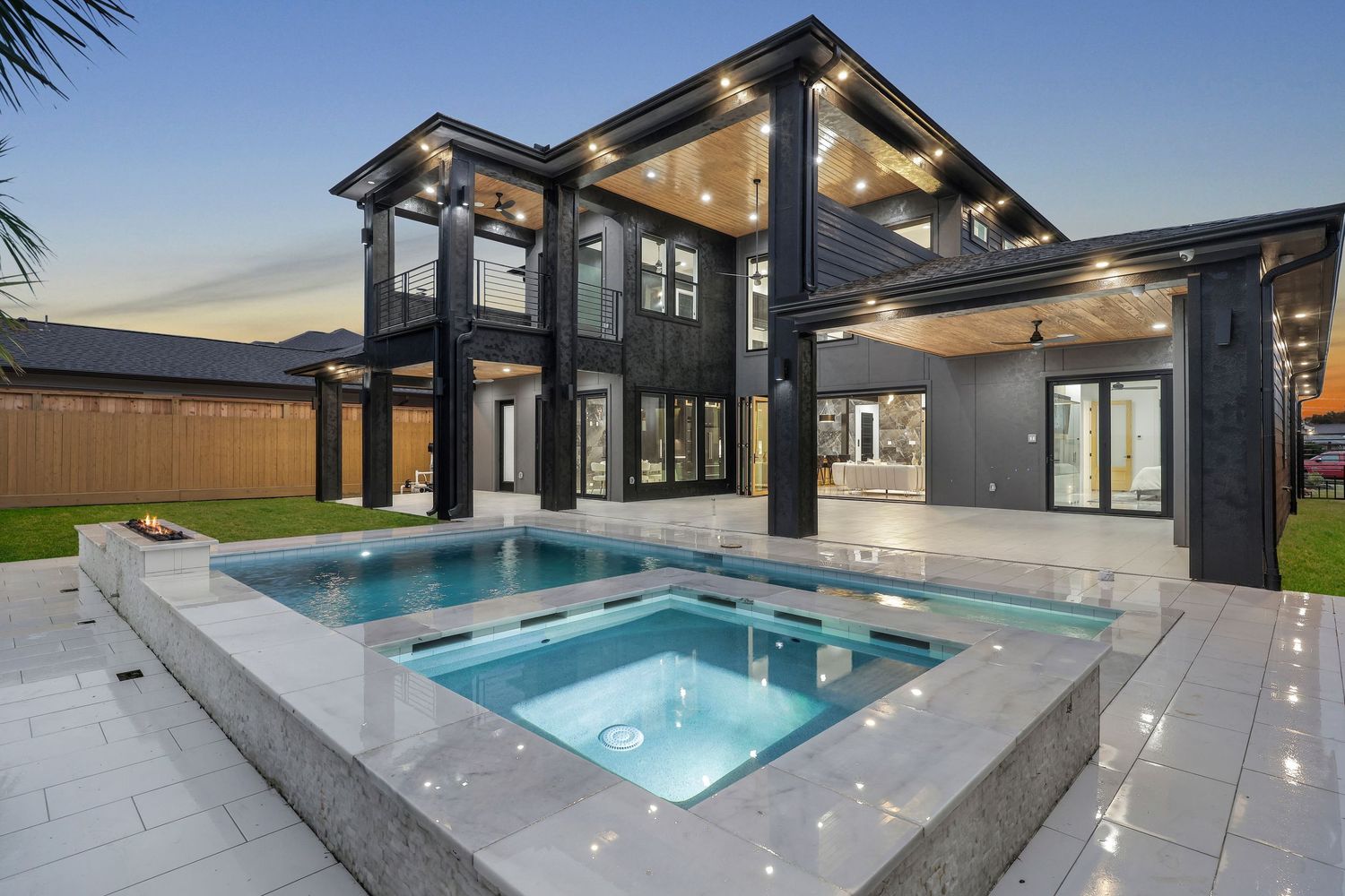 Modern luxury home exterior with infinity pool and hot tub at twilight featuring black structural columns.