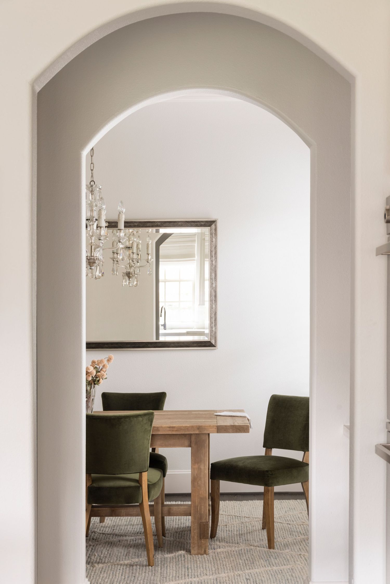 Elegant white archways lead into a minimalist room with wooden furniture and olive green accent chairs.