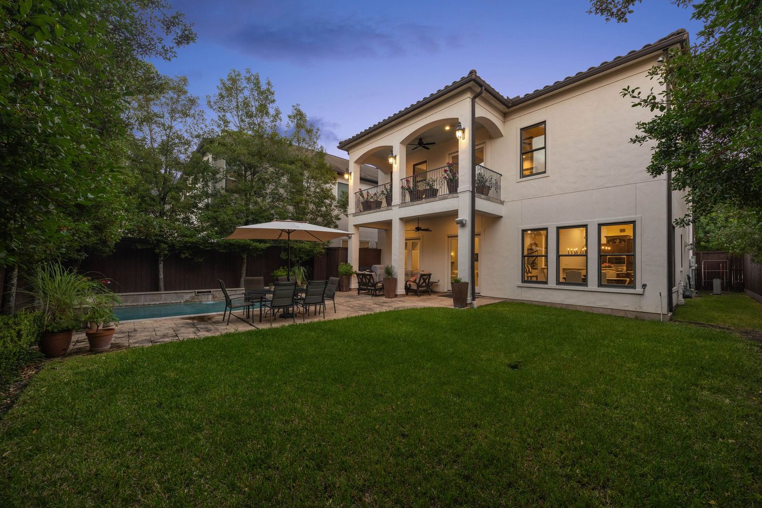 Expansive backyard lawn of luxury home with mature trees and landscaping at twilight.