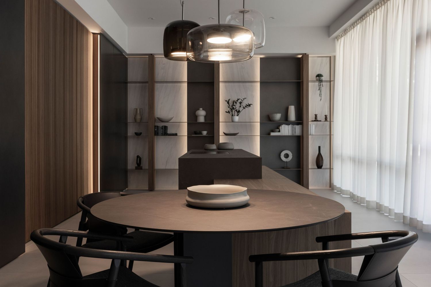 Contemporary dining space featuring sleek pendant lights and dark furniture against white walls.