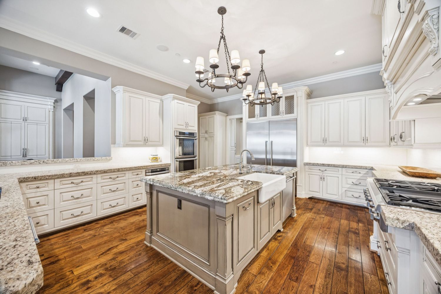 Modern white kitchen with custom cabinetry, hardwood floors, and elegant lighting fixtures.