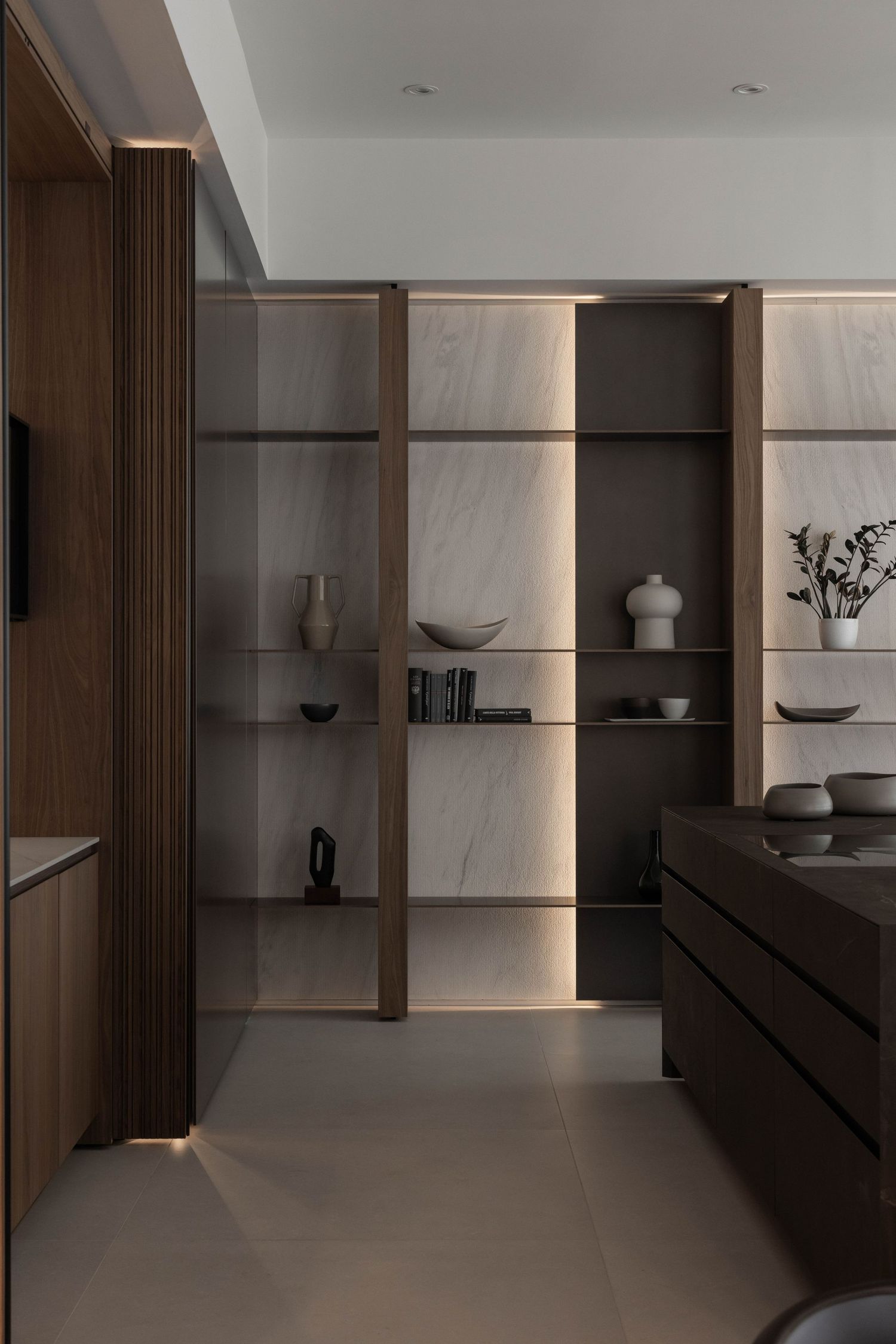 Built-in wall unit with illuminated shelving displaying modern decorative objects and ceramics.