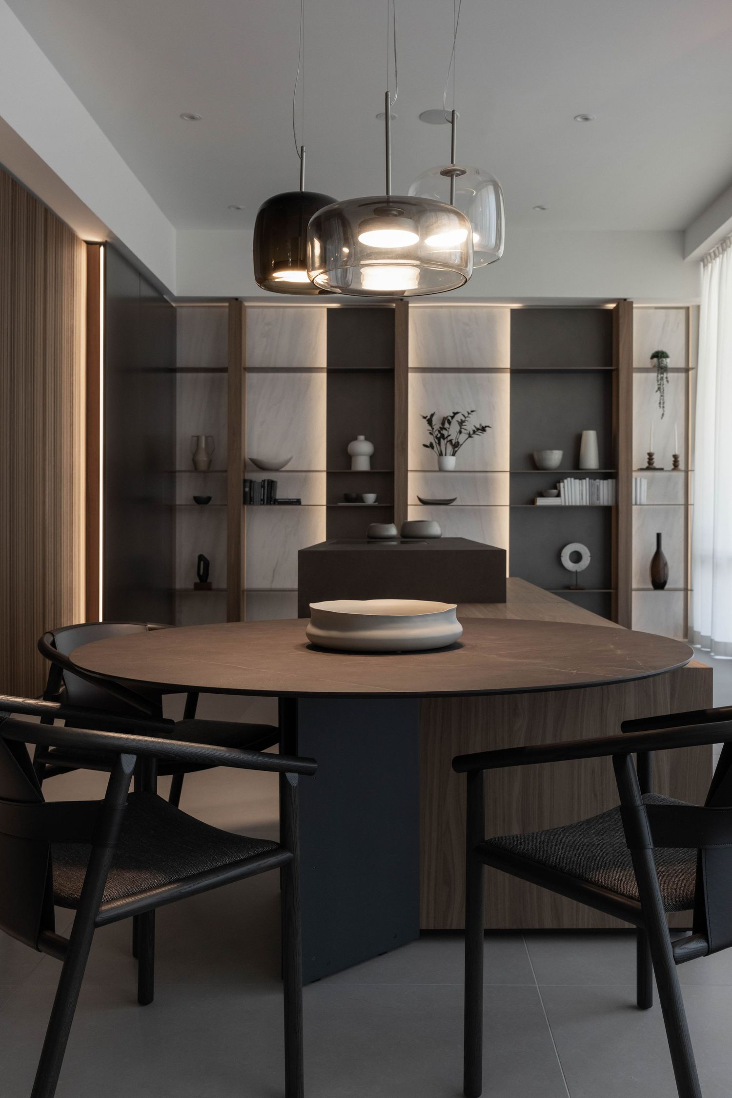 Stylish dining setup with wooden round table, black chairs and decorative wall shelving.