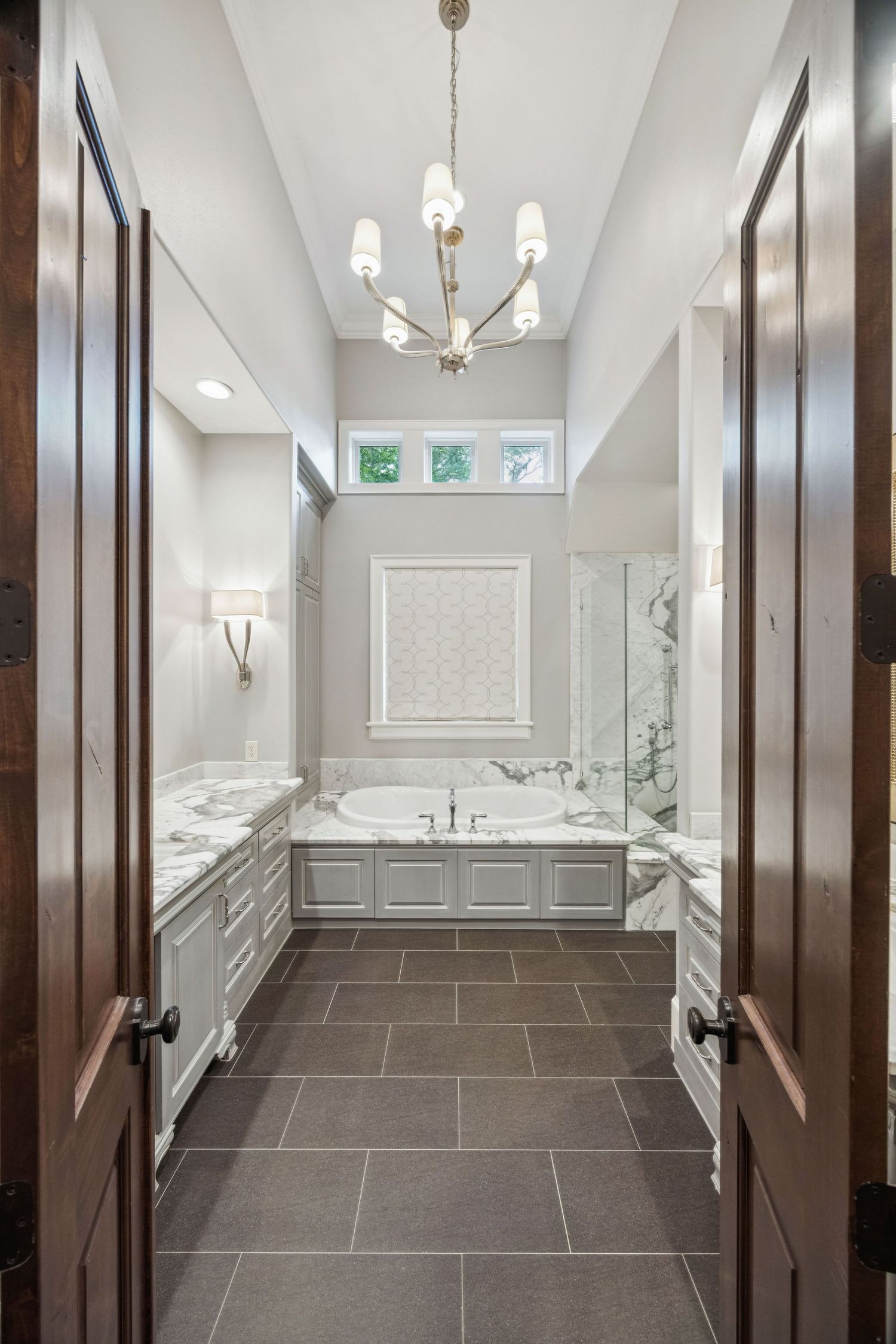 Elegant bathroom interior with dark tile floors, white walls, and chandelier lighting fixtures.